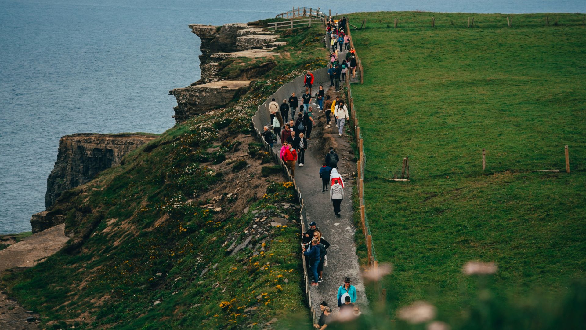 Tourists walk along a cliff path beside the ocean.