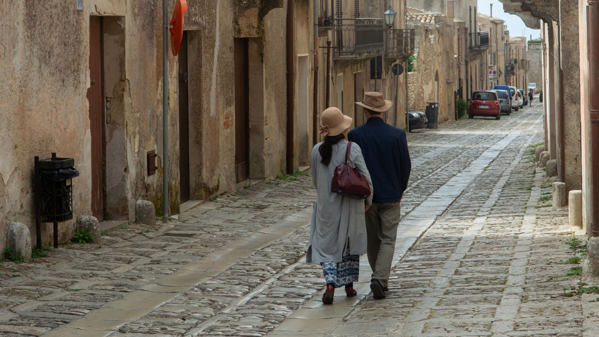 Couple walking on a cobblestone street in Erice, Sicily, showcasing charming historical architecture.