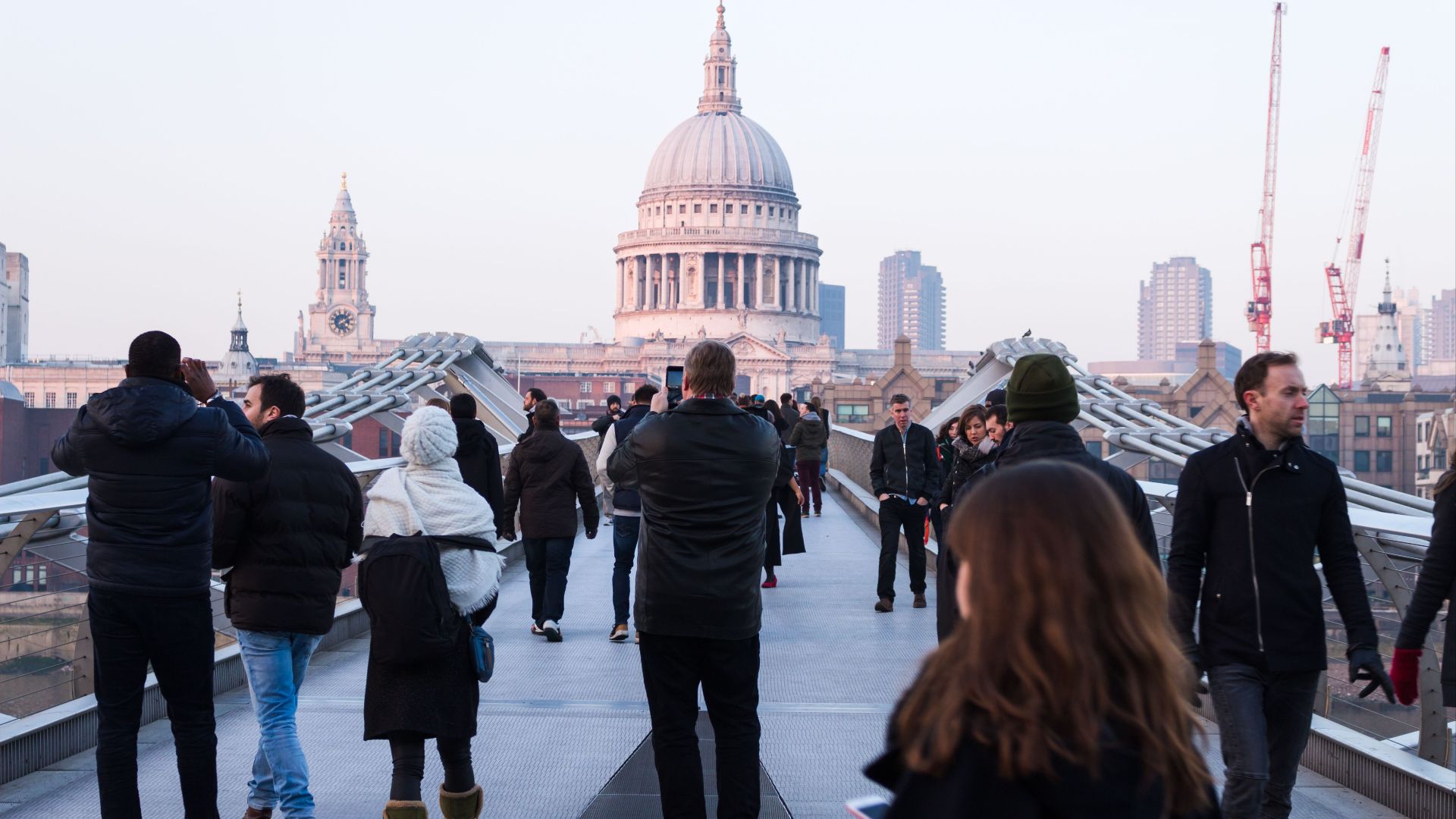 People walking across Millennium Bridge towards St Paul's Cathedral in London with a cityscape background.