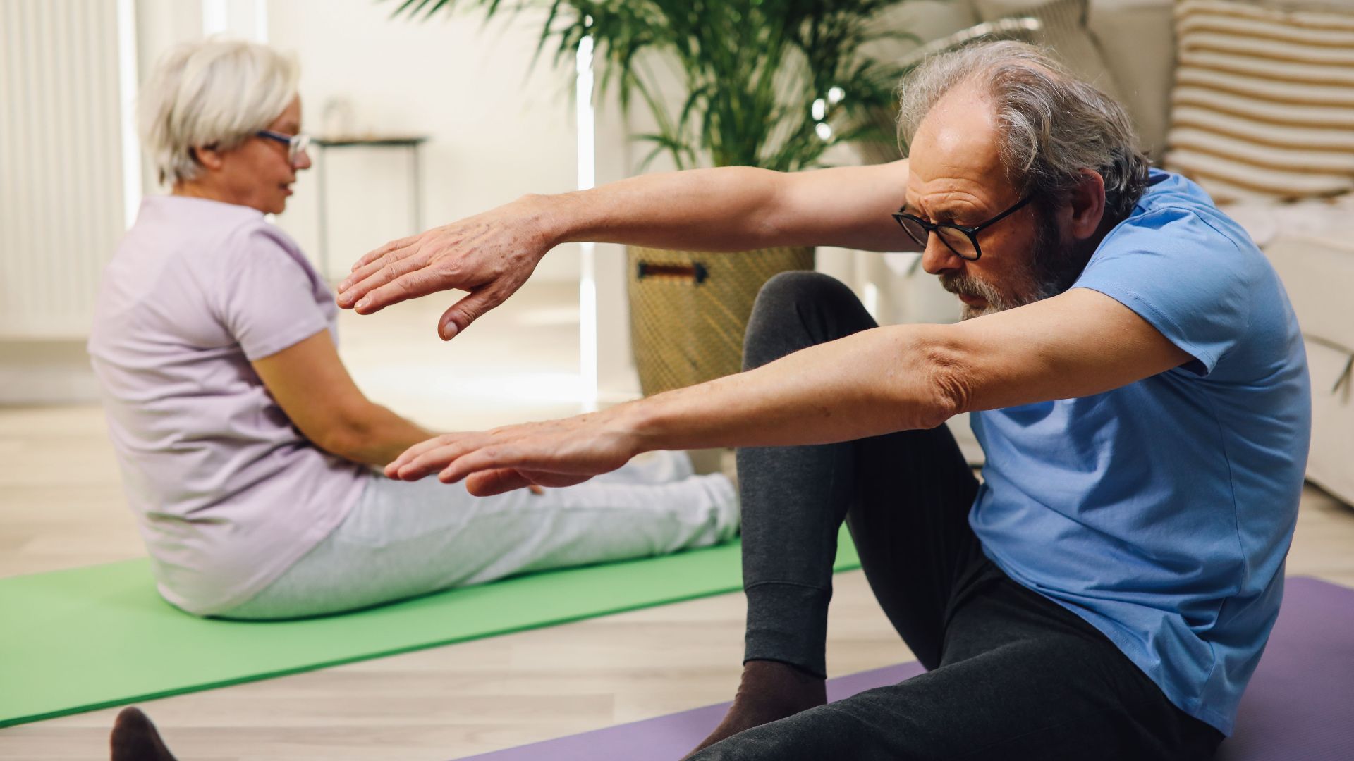 Elderly couple practicing yoga indoors with focus on wellness and fitness.