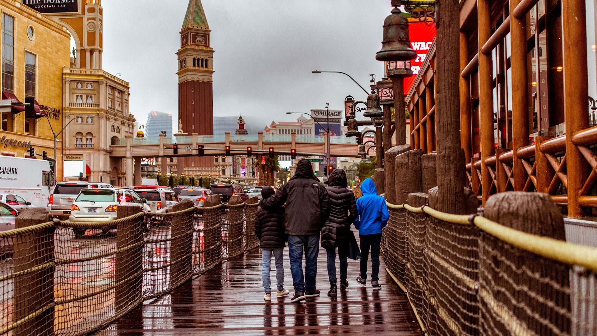People walking along a wet street in Las Vegas with iconic architecture and a cloudy sky.