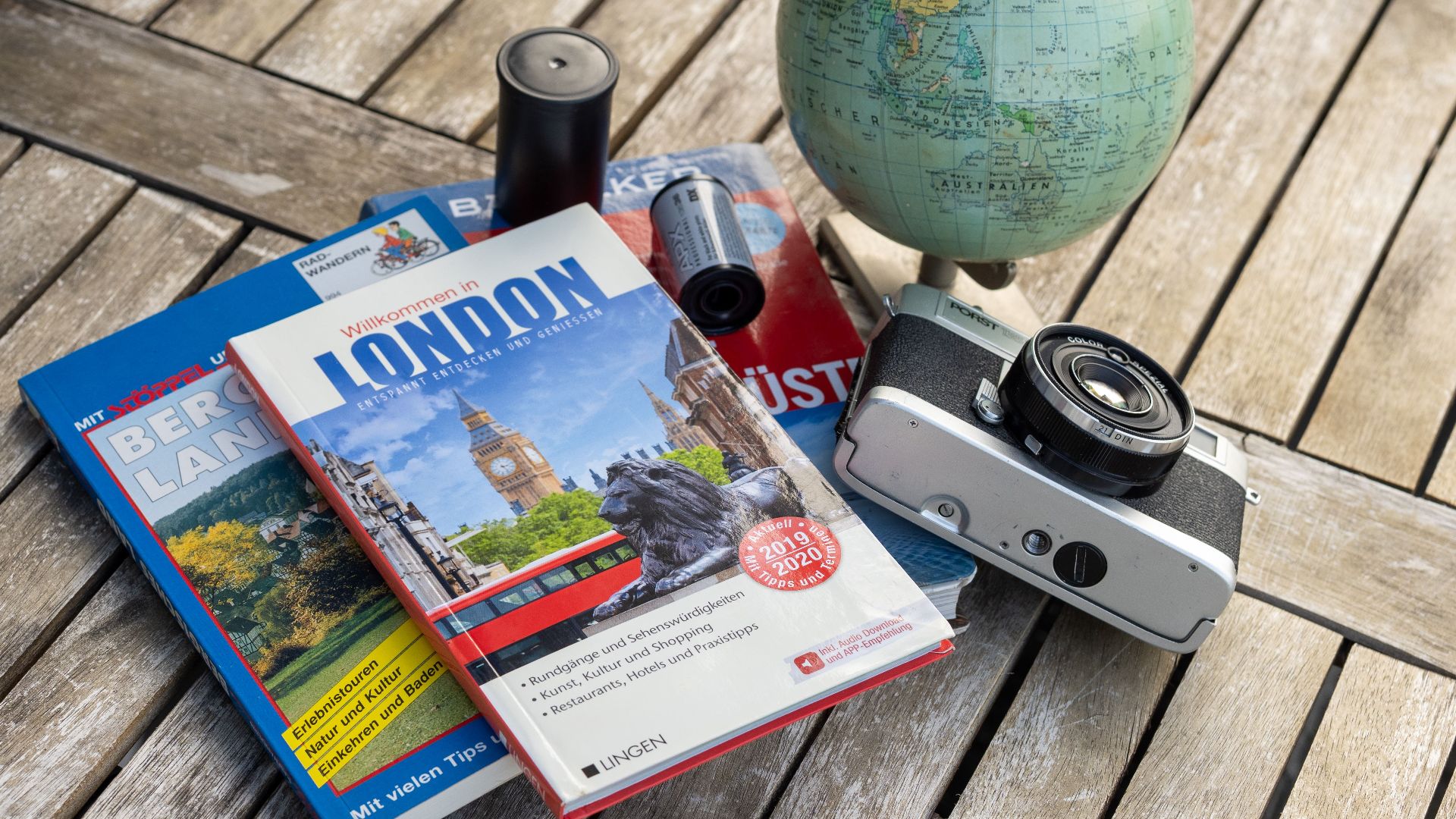 A vintage travel setup with guidebooks, a globe, and a film camera on a wooden table.
