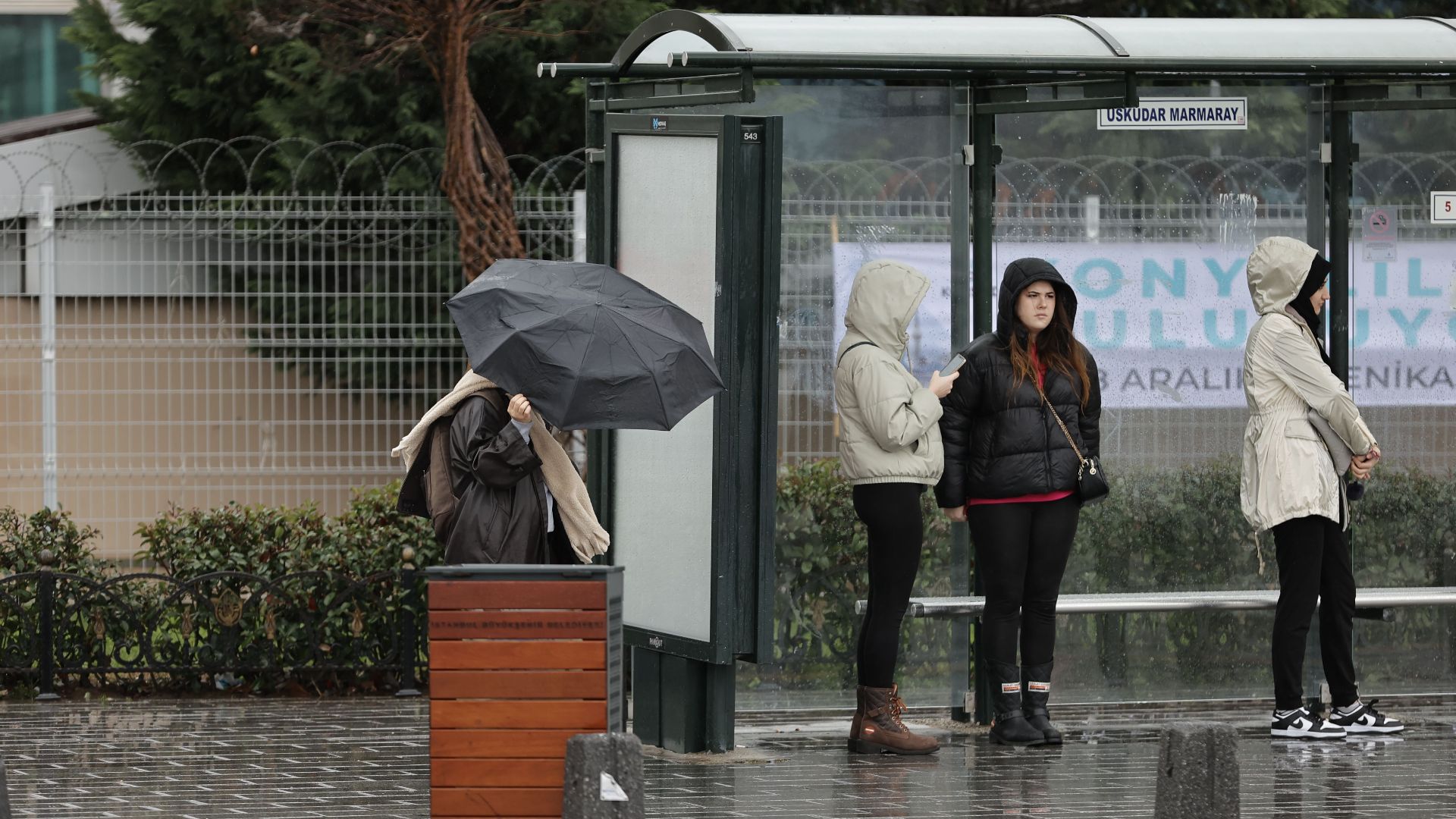 A rainy day at Üsküdar Marmaray station in Istanbul, with people waiting under umbrellas.