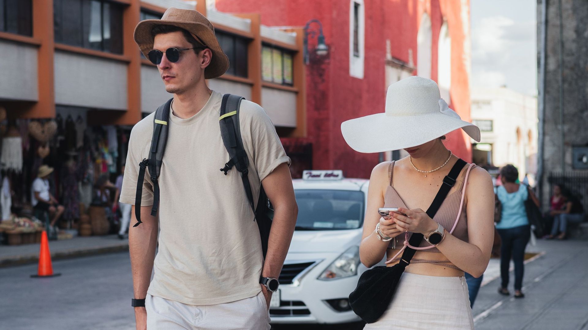 Couple walking along a vibrant street beside a historic red building under blue skies.