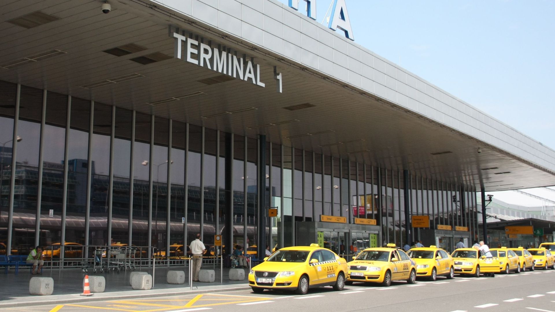 Exterior view of Praha Airport's Terminal 1 with a line of yellow taxis awaiting passengers.