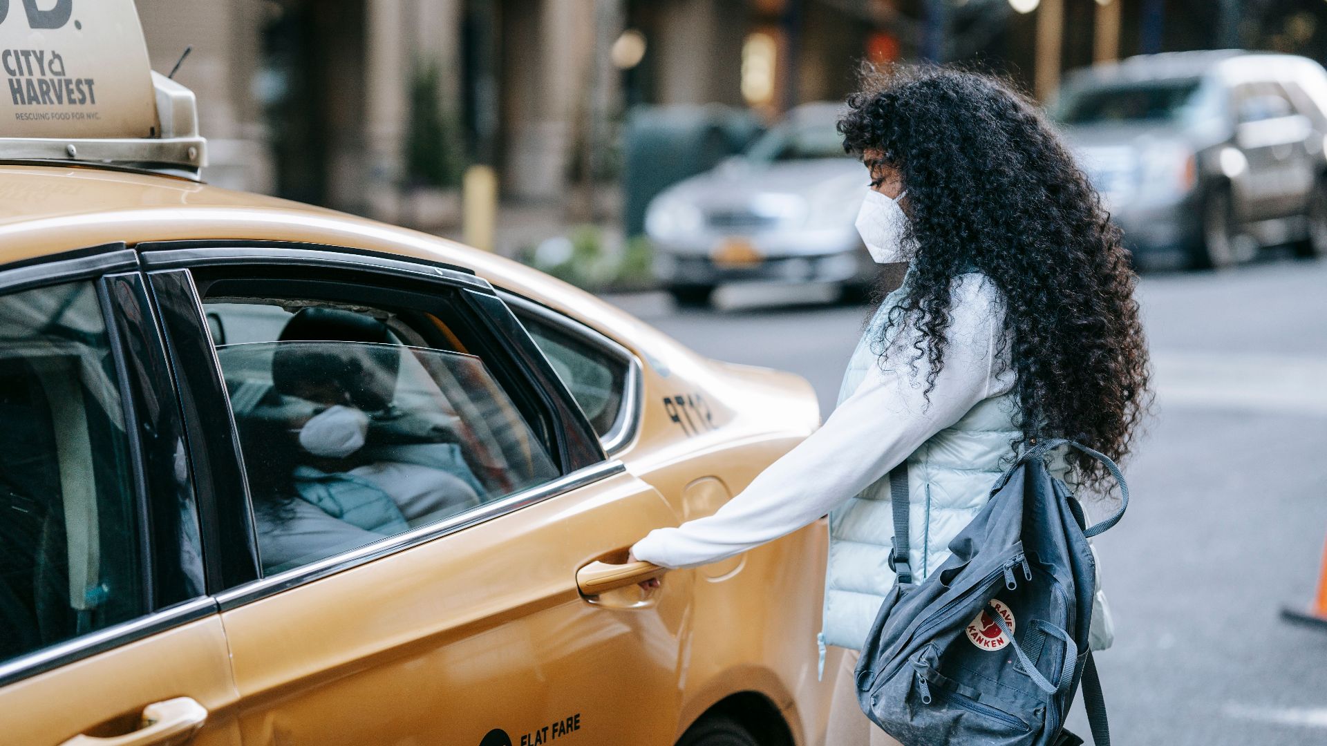 Side view of unrecognizable African American lady with long dark hair in casual clothes and medical mask opening door of ta parked on city street