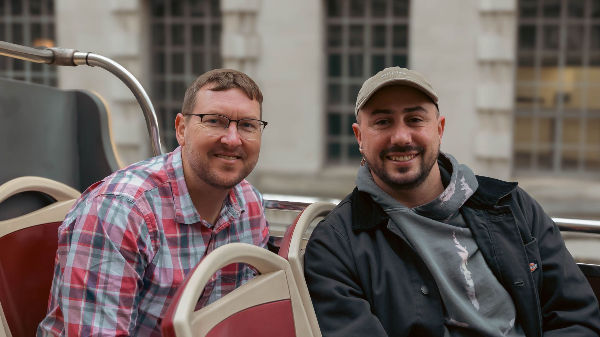Two adults on a London sightseeing bus tour. Outdoor urban setting.