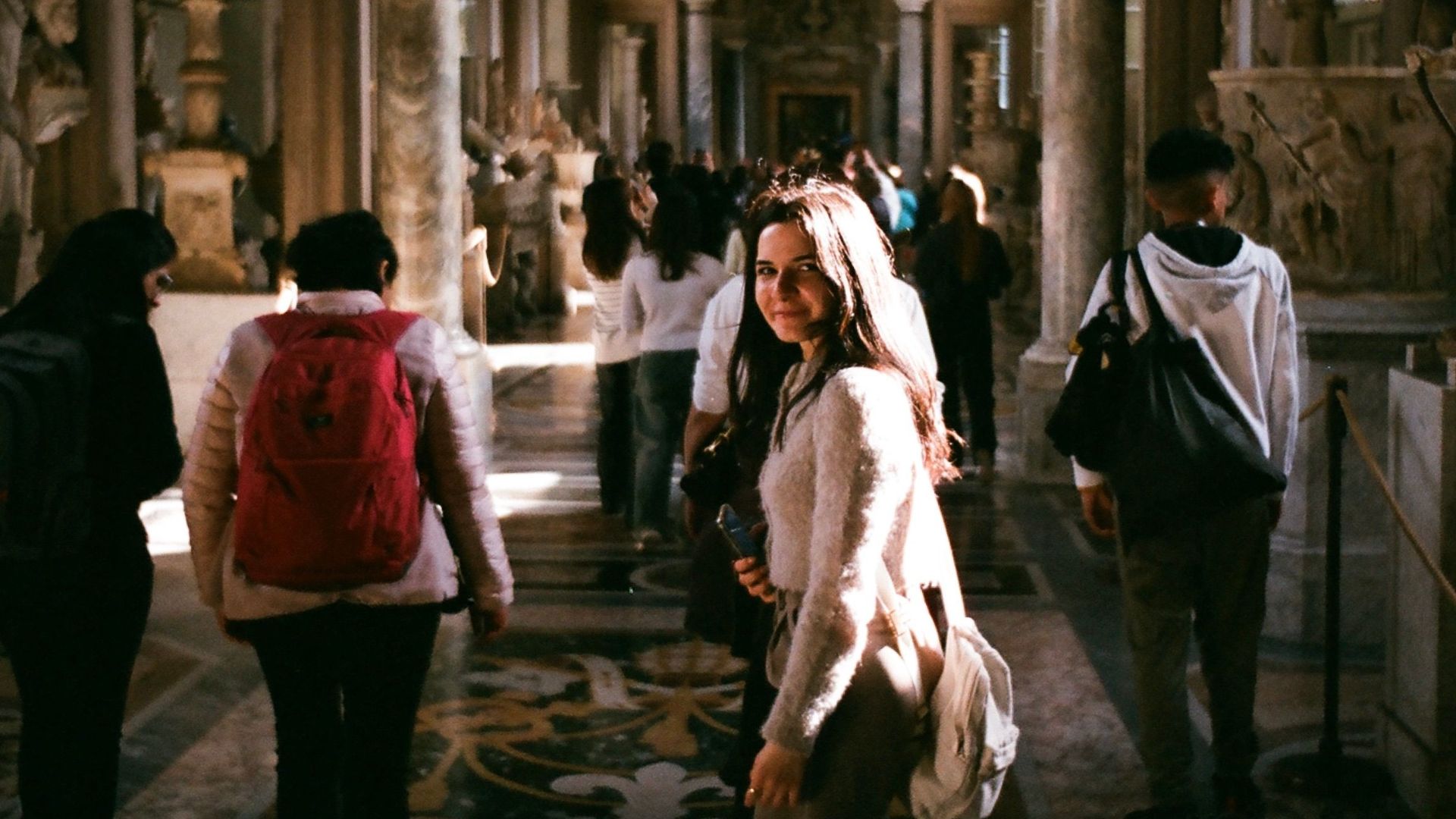Tourists exploring the historic corridors of the Vatican Museums, surrounded by ancient sculptures and art.