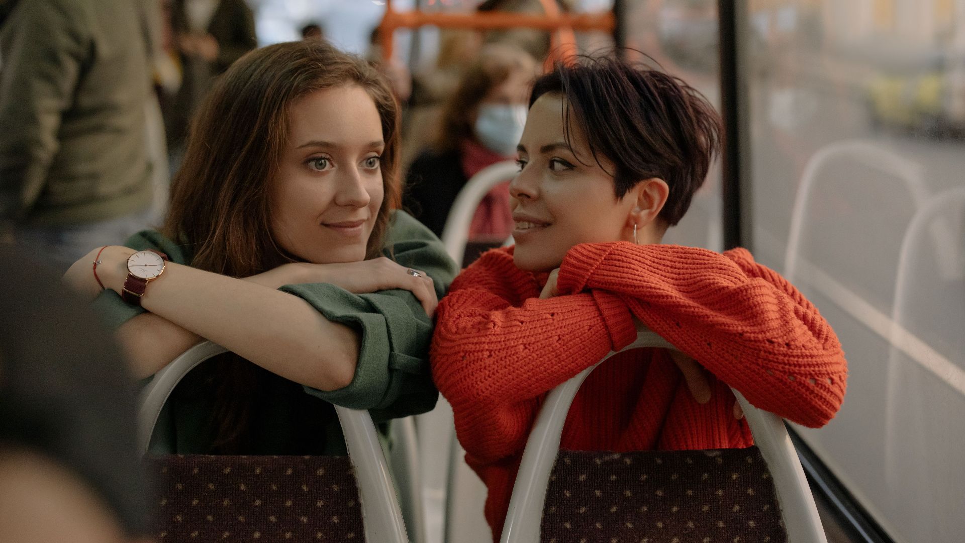 Two young women enjoy a friendly conversation while traveling on a city bus.