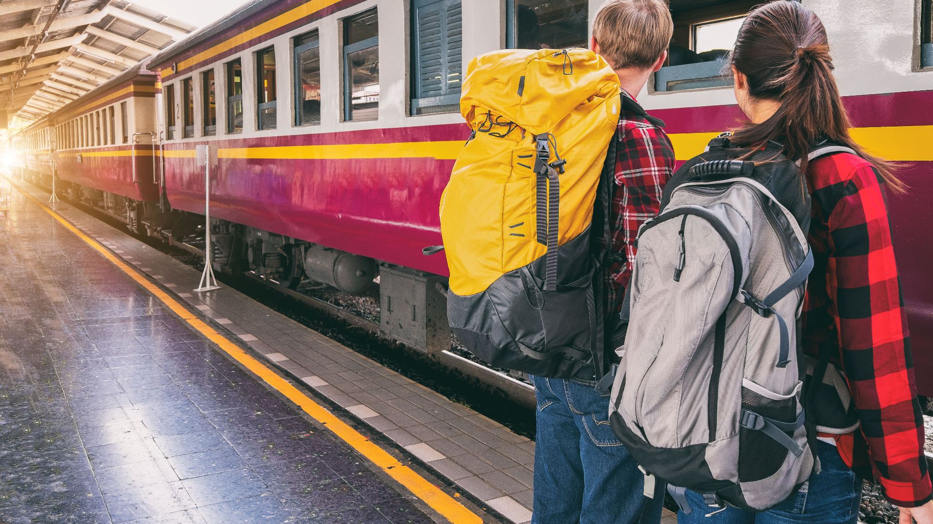 Backpackers waiting at a train station platform, ready for travel adventure.