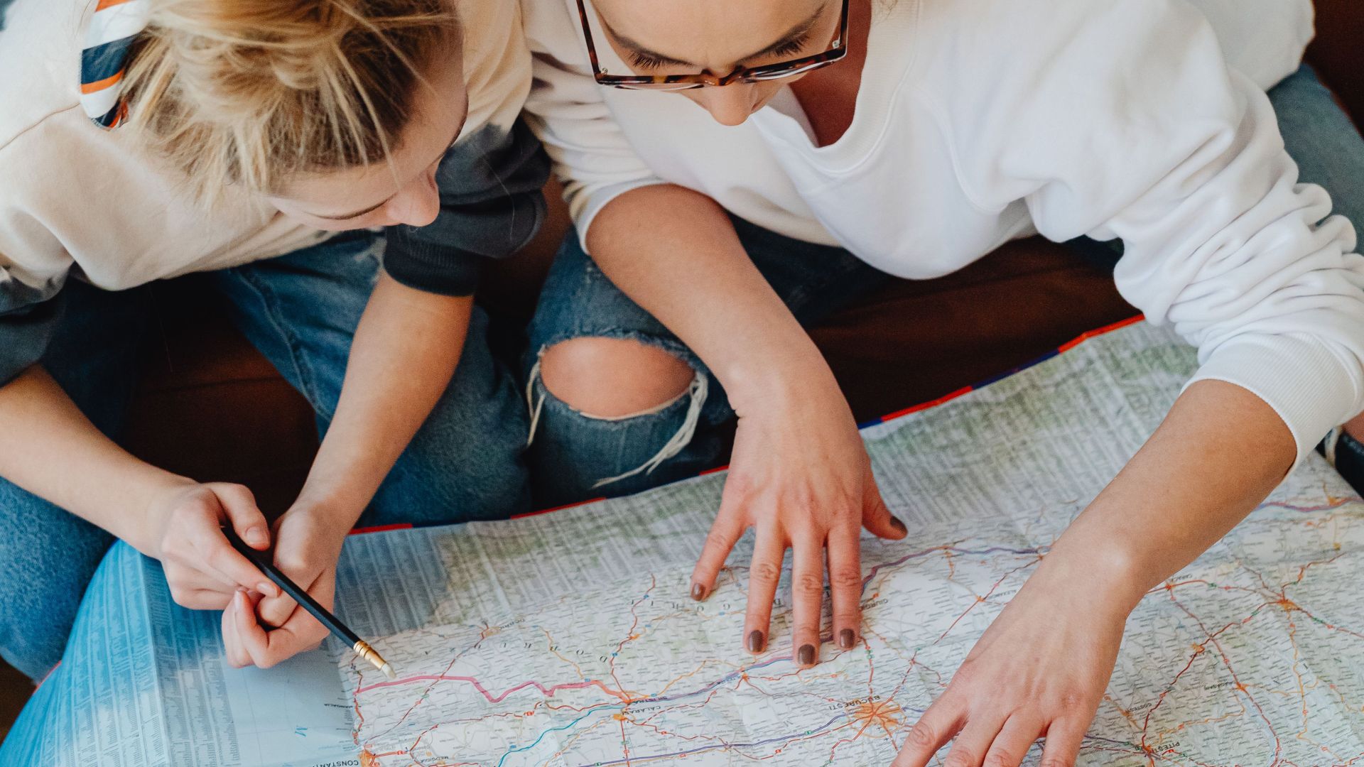A mother and daughter planning a trip using a map while sitting on a sofa.