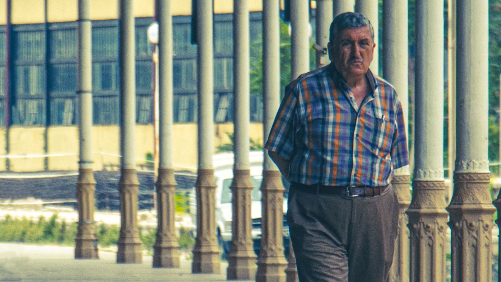 An elderly man strolls through a historic corridor lined with columns.
