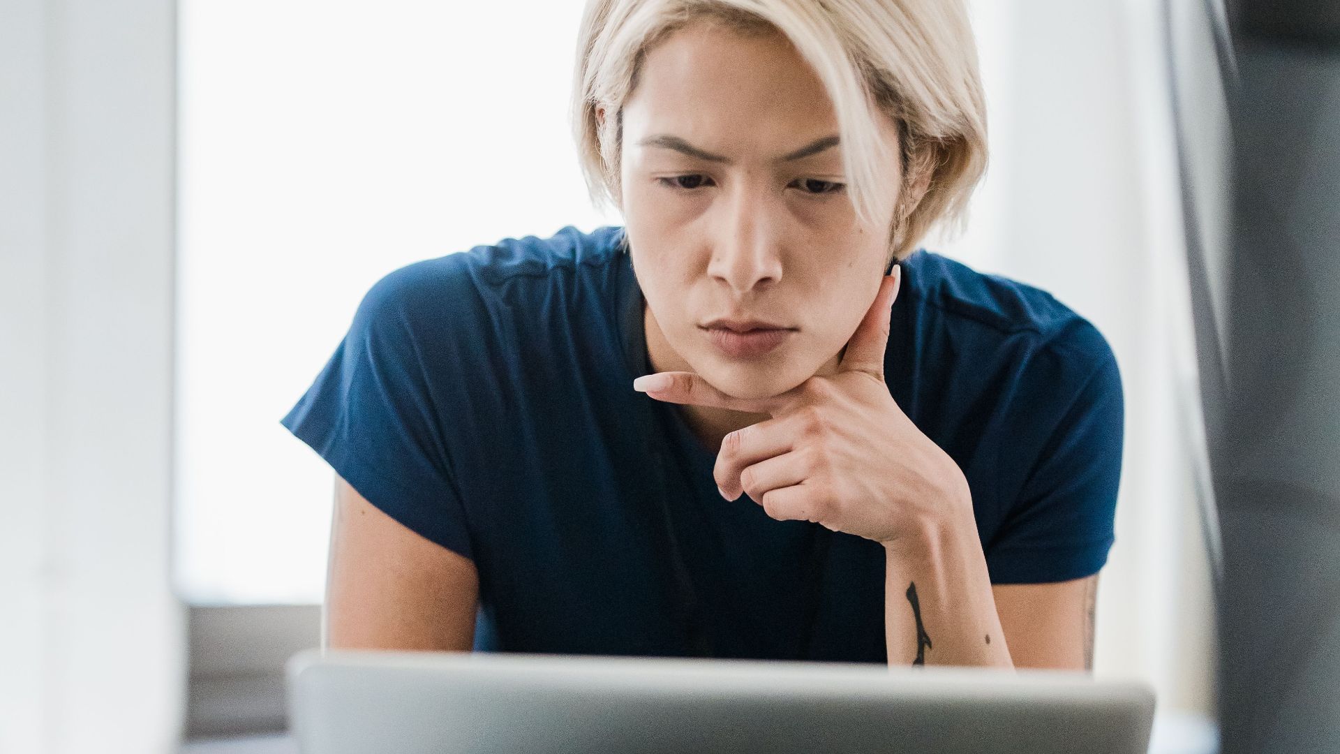 Young woman concentrating while working on a laptop in a bright office setting, representing productivity and focus.