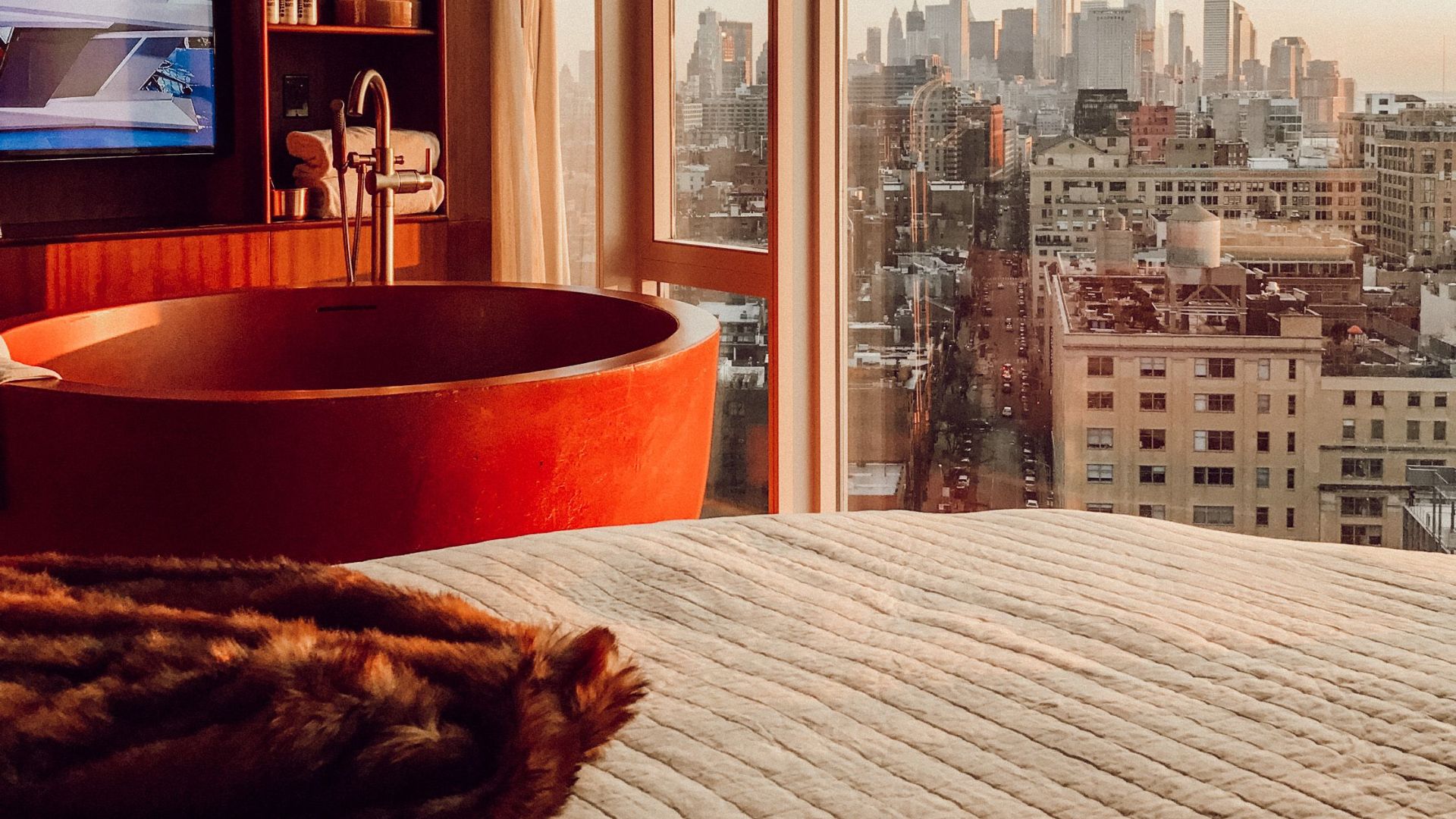 Elegant hotel room featuring a bathtub with cityscape view, capturing an urban sunset.