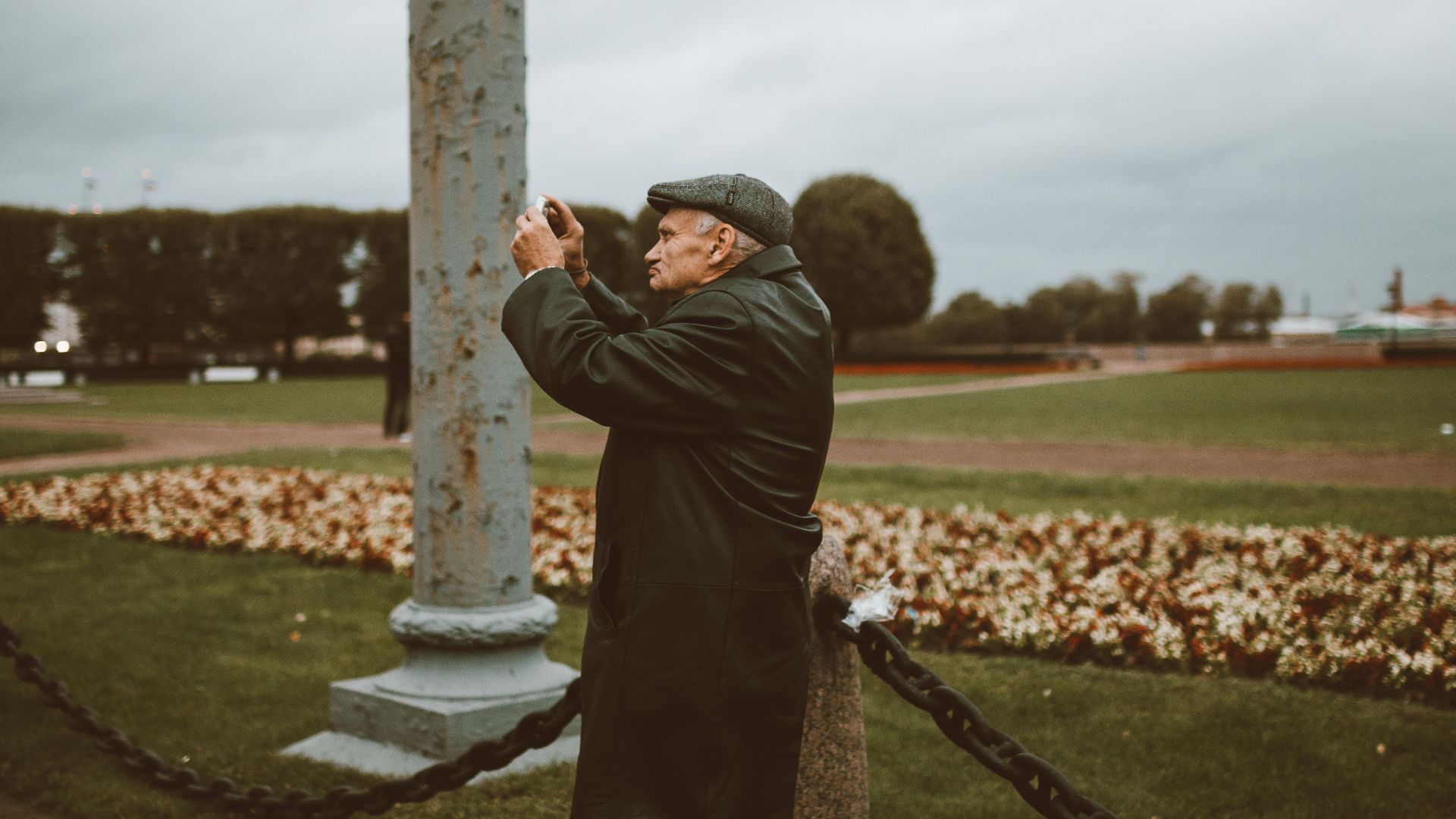 Senior man uses a smartphone camera to capture nature in a Russian park.