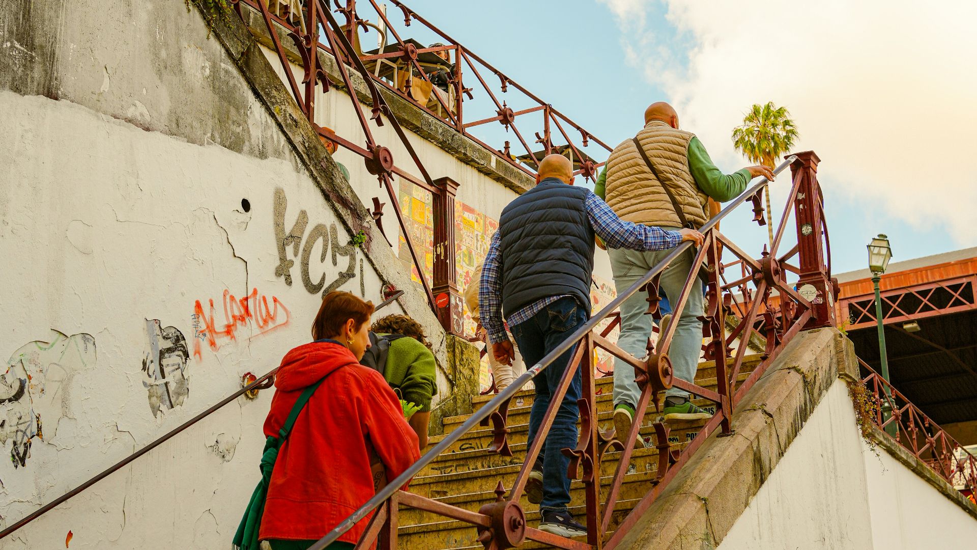 People climb a steep outdoor staircase under a cloudy sky.