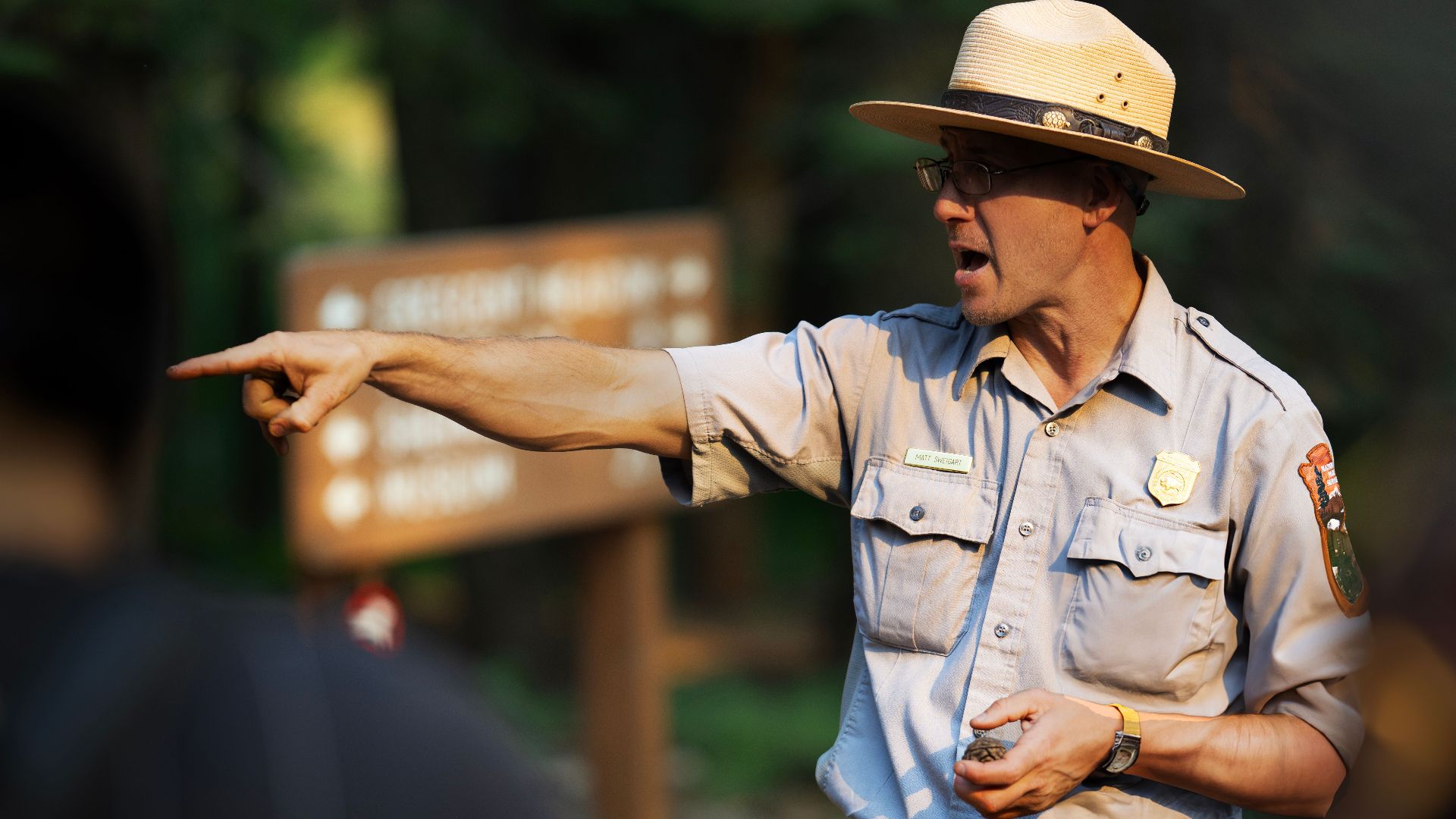 Park ranger guiding a group through a forest area, pointing with emphasis.
