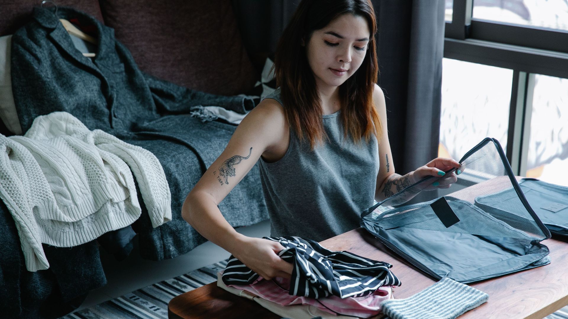 A young woman organizing her clothes in a cozy and modern bedroom, preparing for a trip.