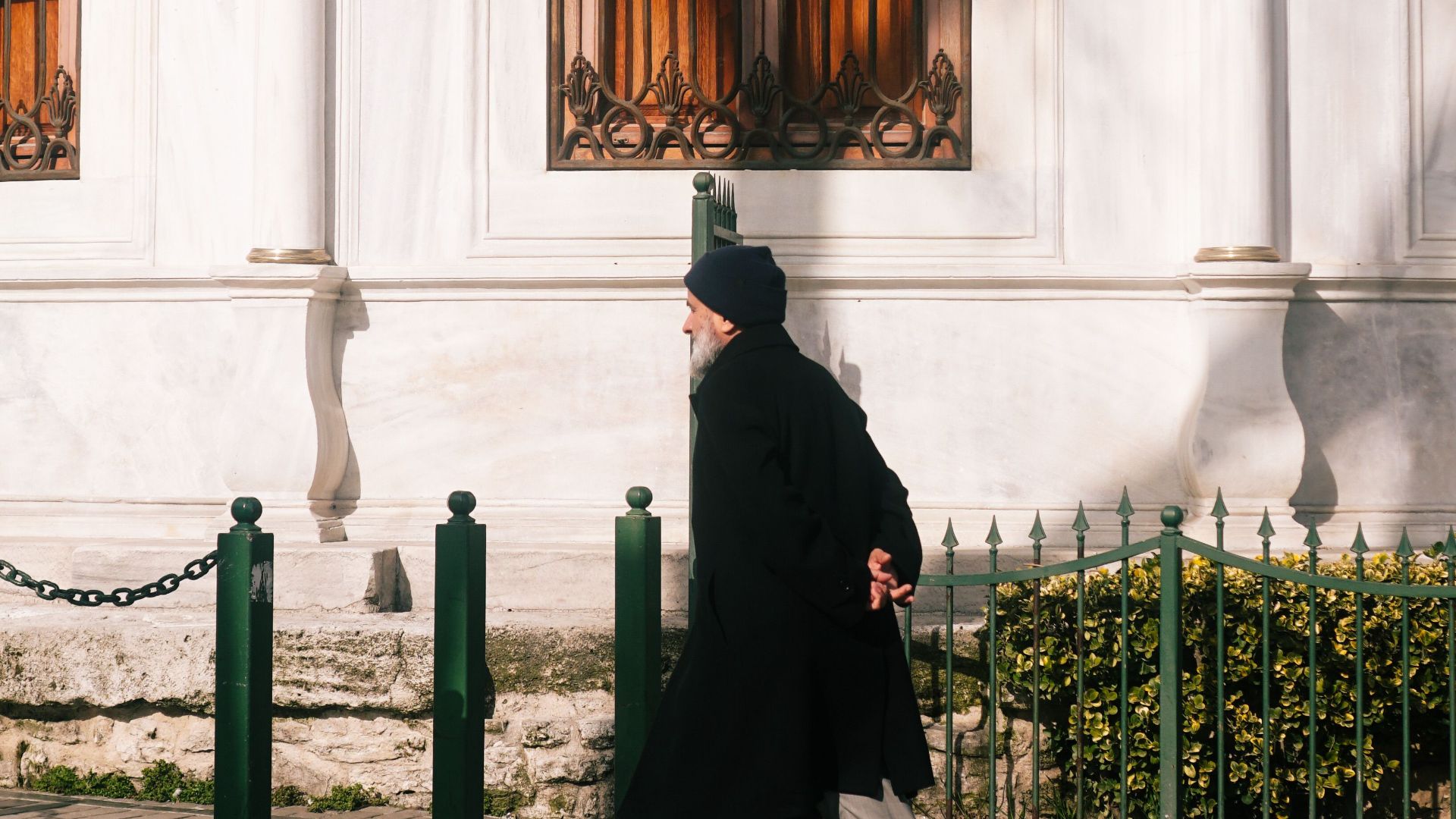 A man in a coat walks past a historical building with intricate wooden windows.