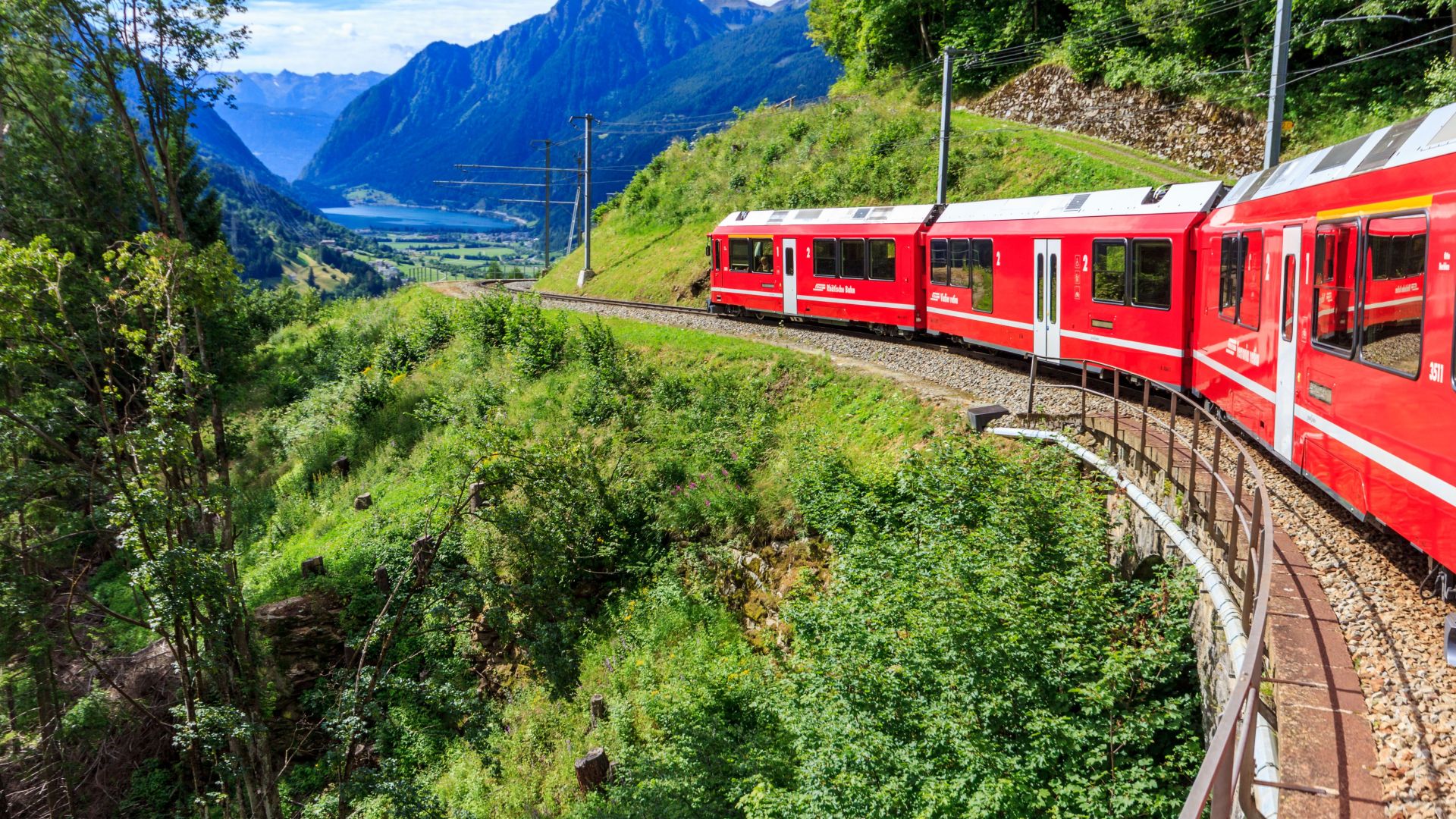 Bernina Express train curves through the stunning Swiss Alps, offering breathtaking views of mountains and valleys.