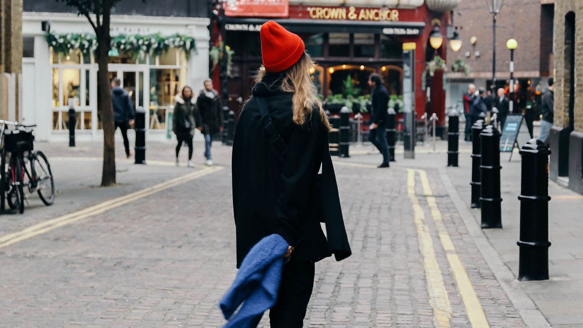 Woman strolling on a quaint London street with historic architecture and cobblestone pavement.