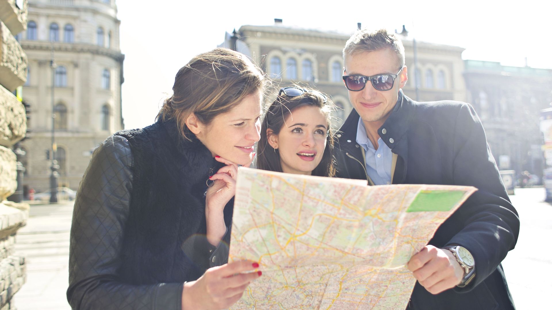 Three tourists exploring a city using a map under bright daylight, enjoying their travel journey.