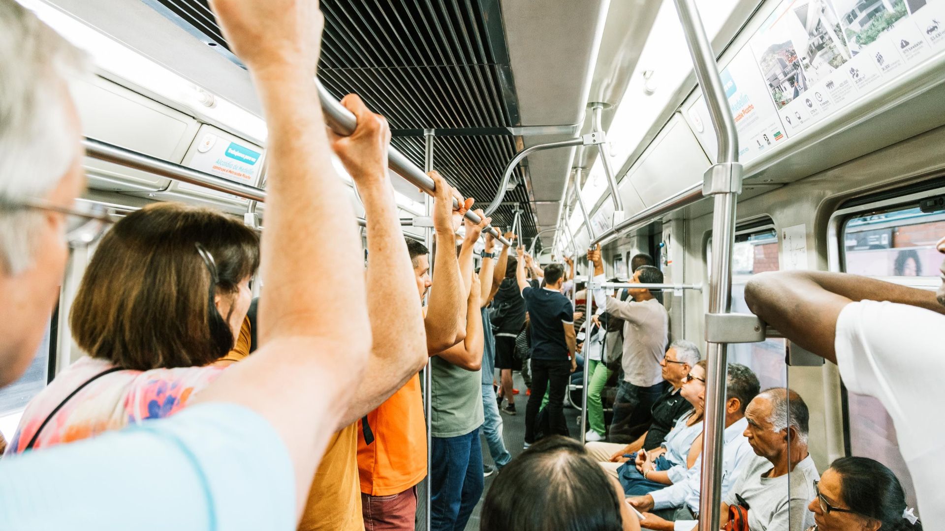 Metro train with sitting and standing passengers with hands on handrail during busy day in town