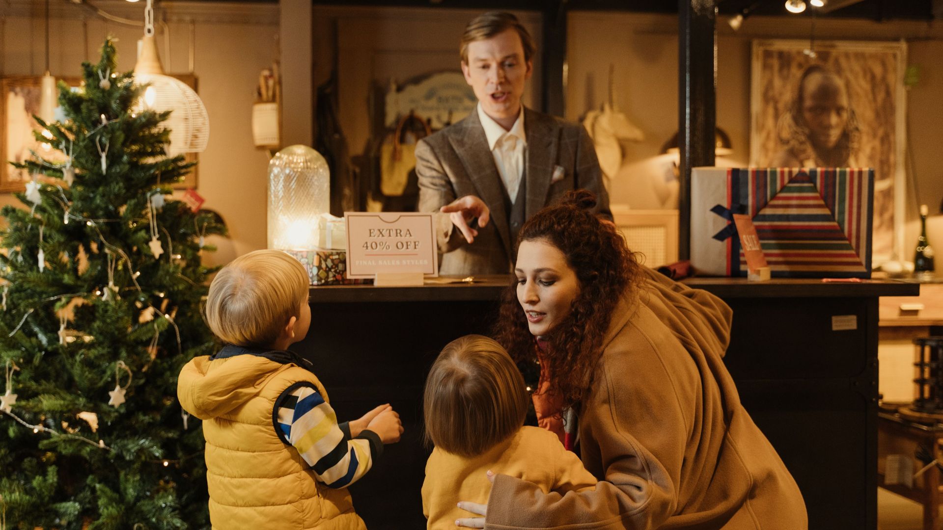 A family shopping during the holiday season with children near a Christmas tree seeking great deals.
