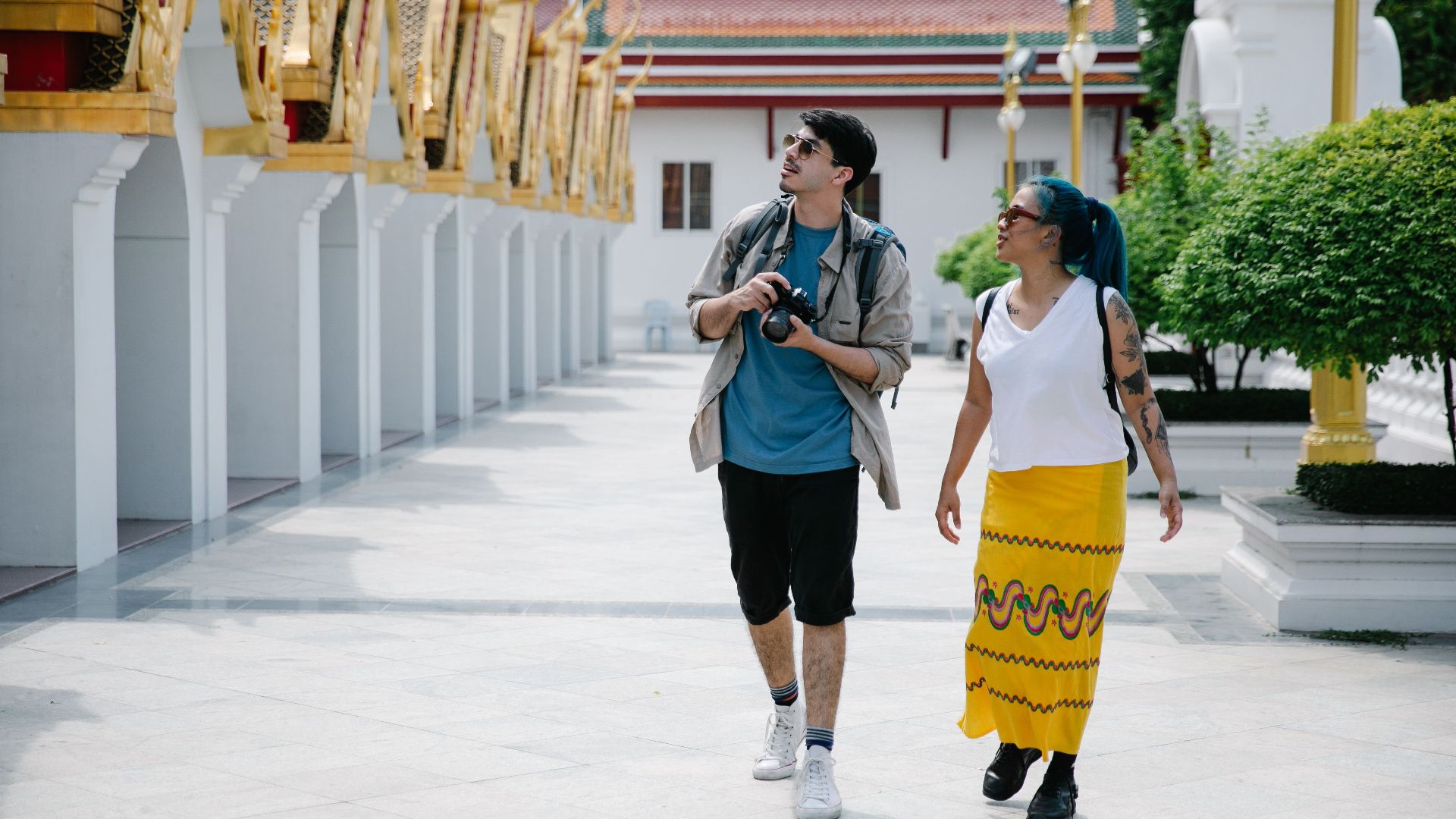 Two tourists walk and explore a traditional Thai temple, enjoying sightseeing and photography.
