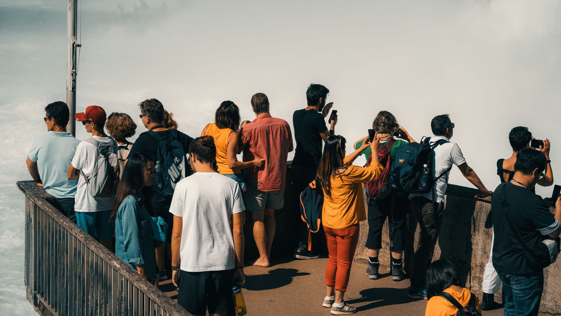 Group of tourists capturing the majestic Rhine Falls from a viewing platform in Switzerland.