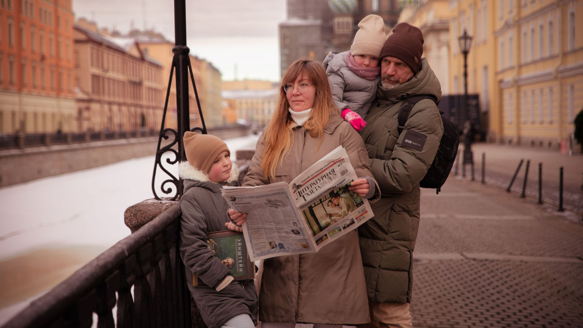 A family strolls along a canal in Saint Petersburg on a winter day, bundled up warmly against the cold.