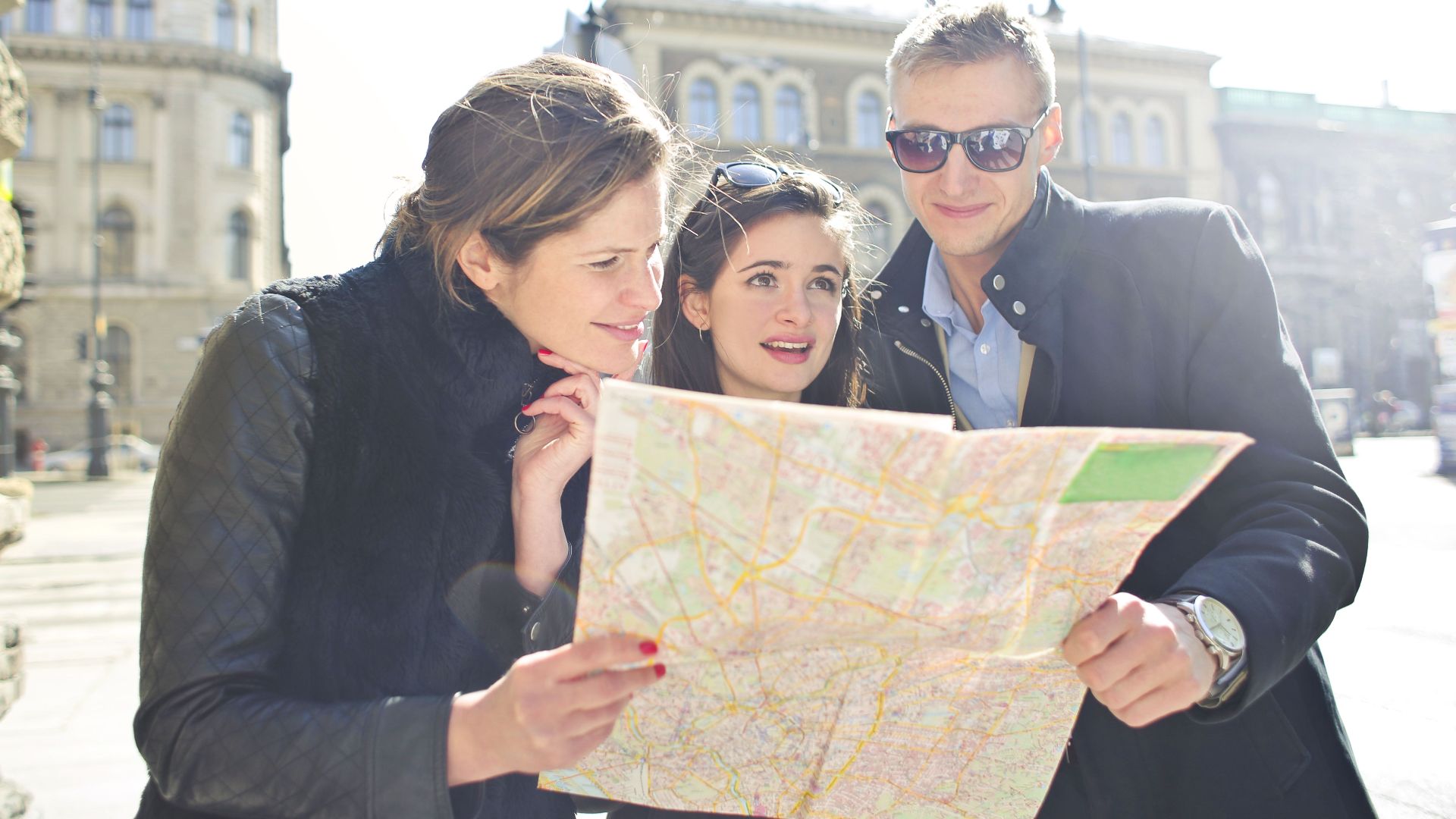 Three tourists exploring a city using a map under bright daylight, enjoying their travel journey.