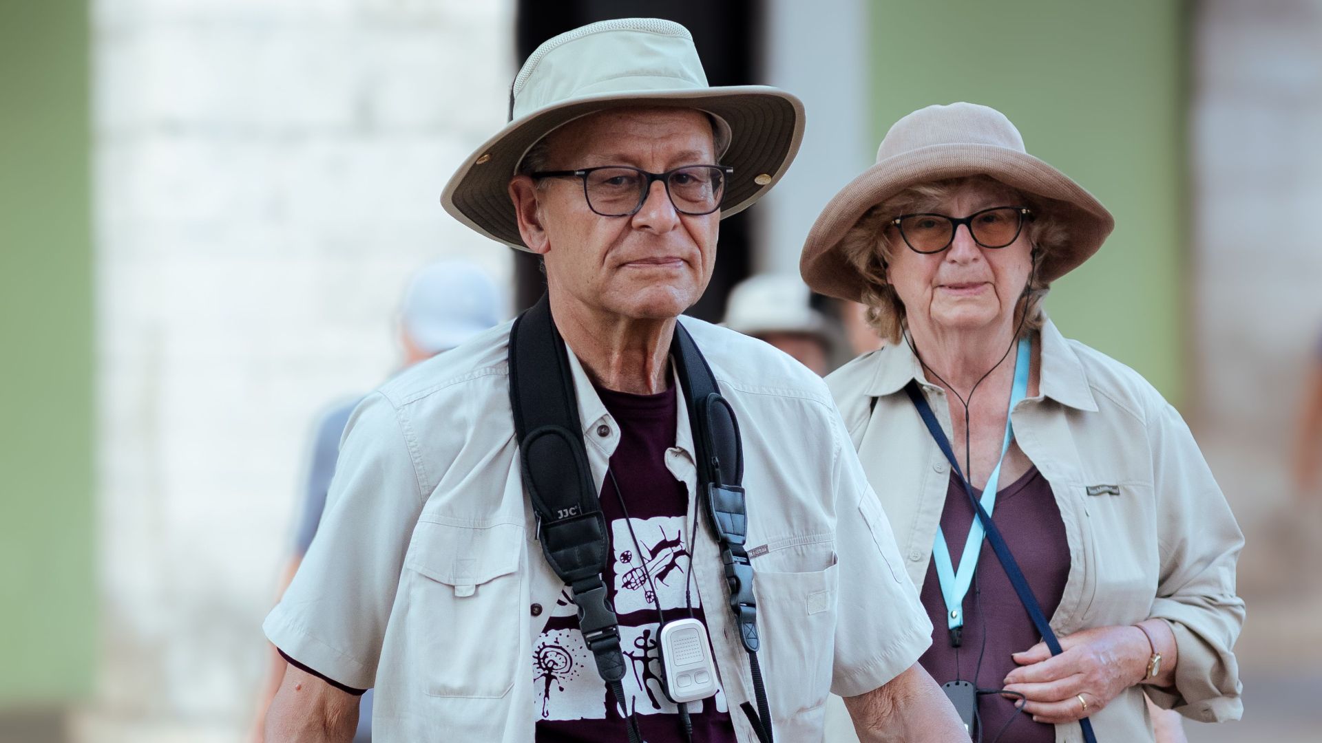 Elderly couple with sun hats and cameras crossing a zebra crossing outdoors.