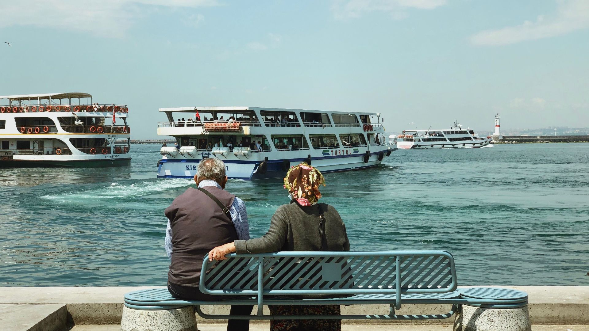 Elderly couple enjoying a calm day by the sea in İstanbul, Turkey with ferries passing by.