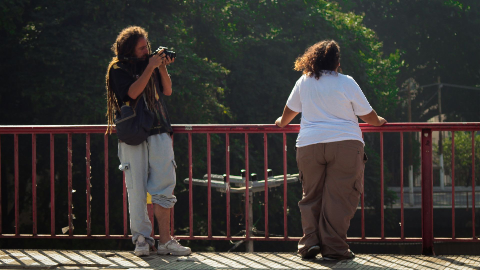 Two people on a bridge, one taking a picture.