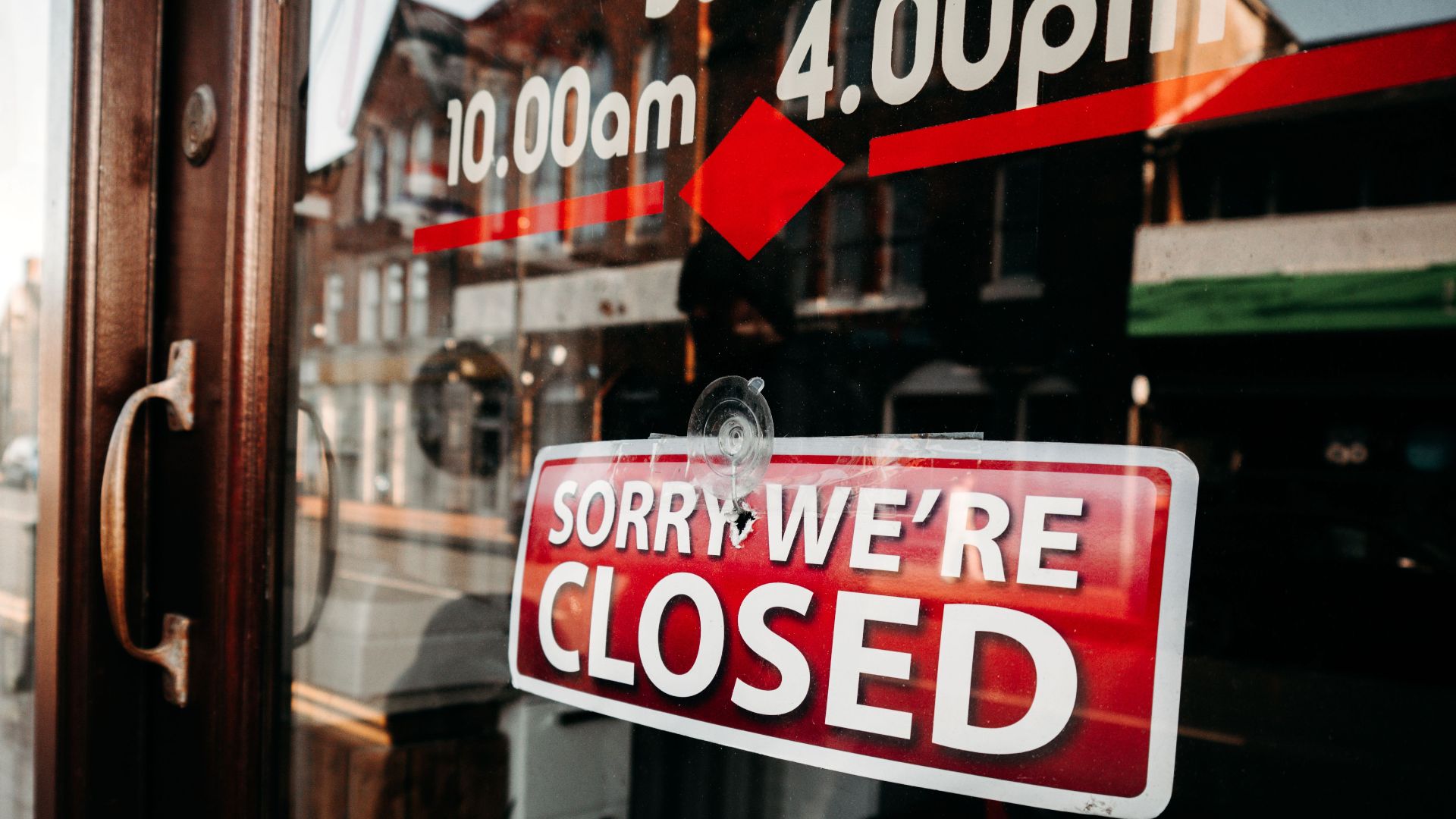 Close-up of a shop's closed sign on a glass door reflecting the street outside.