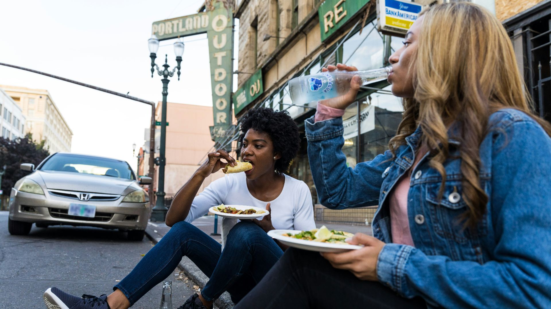 a couple of women sitting on the side of a road eating food
