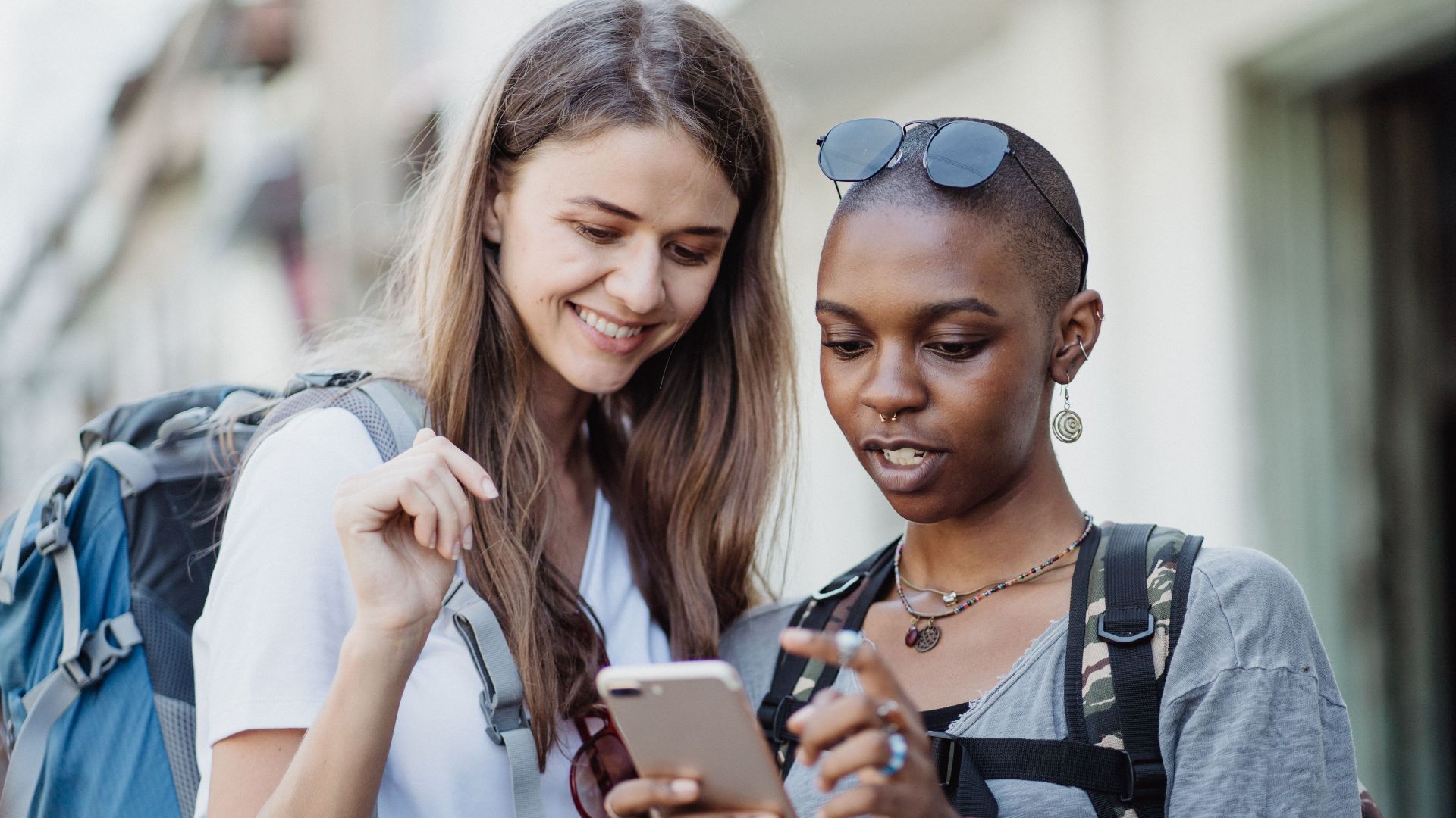 Two friends with backpacks exploring a city, navigating with a smartphone, enjoying a travel experience.