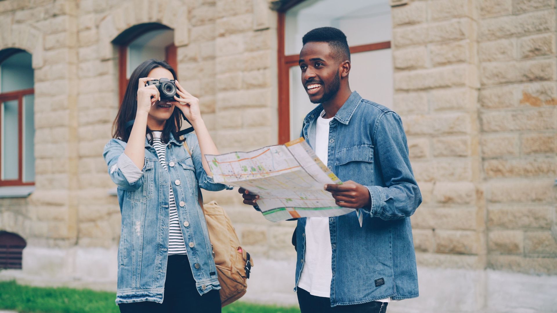 Two smiling tourists with a map and camera exploring a city street in daylight.