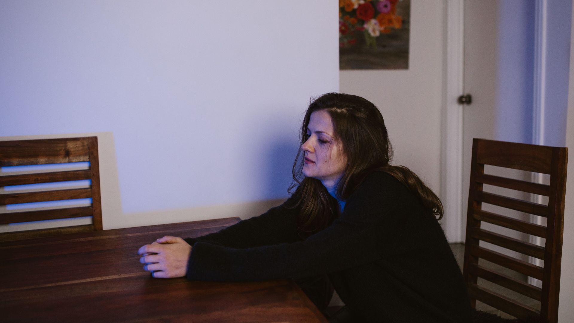 Woman sitting alone at a dining table, contemplating in a dimly lit room.