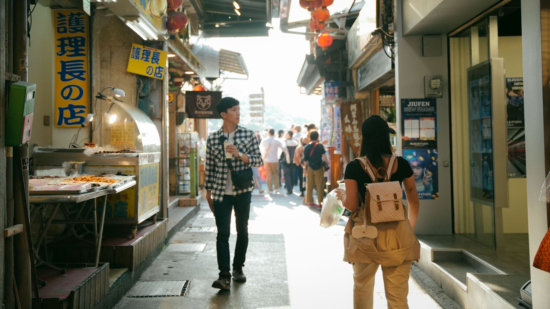 Shoppers exploring vibrant Jiufen street market under sunlight with food stalls and lanterns.