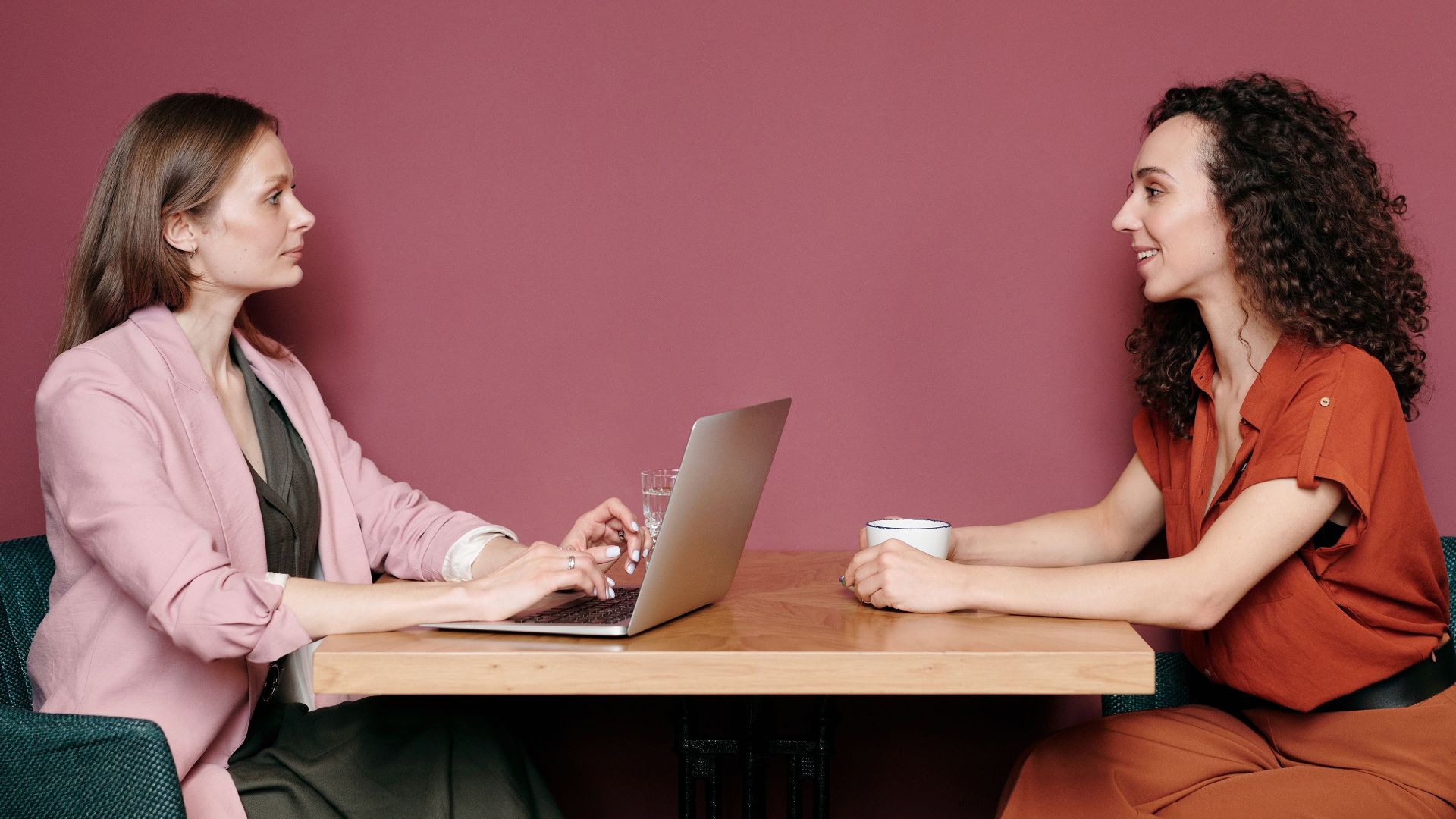 Two women having a meeting at a table with a laptop and coffee inside a stylish room.