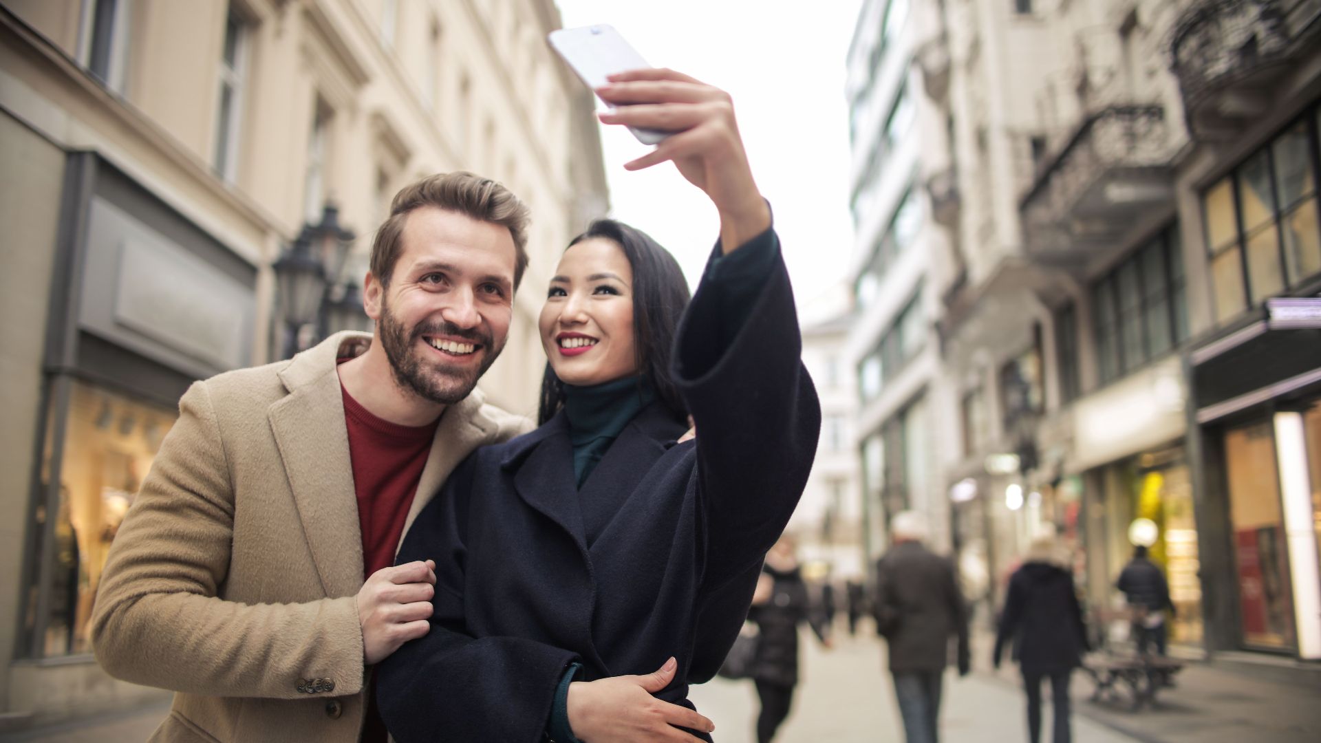 Happy couple takes a selfie on a lively urban street in daylight, capturing joyful moments during their city walk.