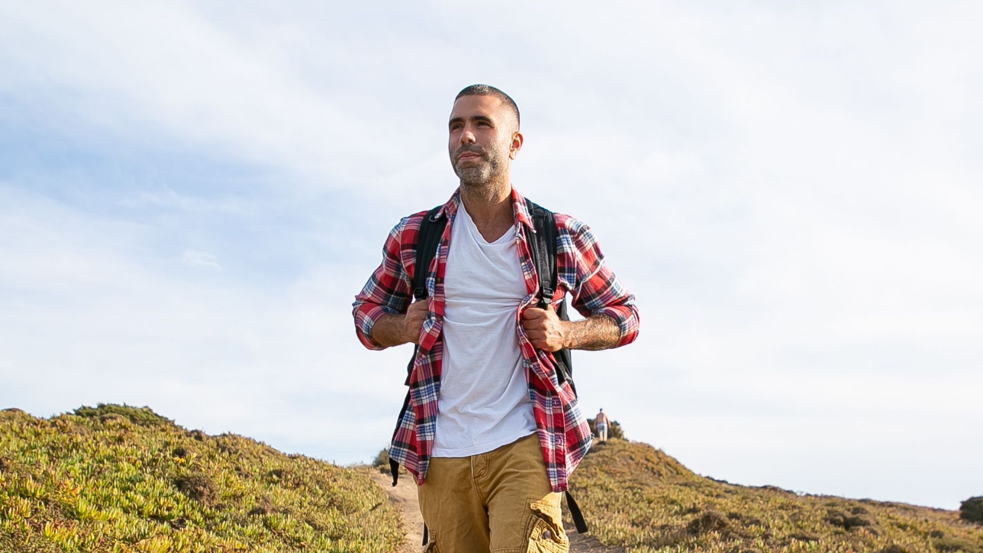 An adult man with a backpack hiking on a sunlit path in Portugal's countryside.