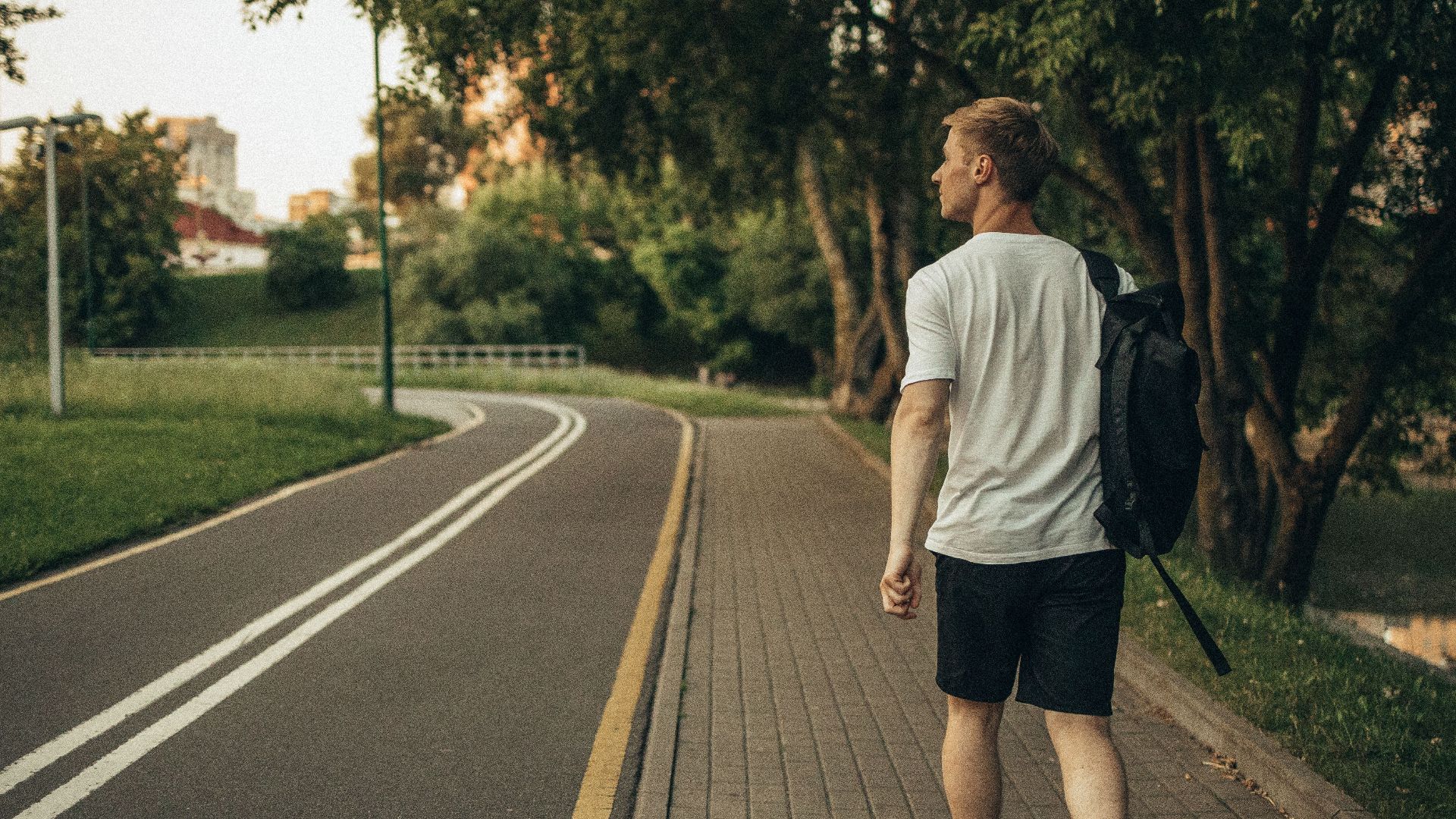 A man walks through a peaceful park on a paved path surrounded by lush greenery.