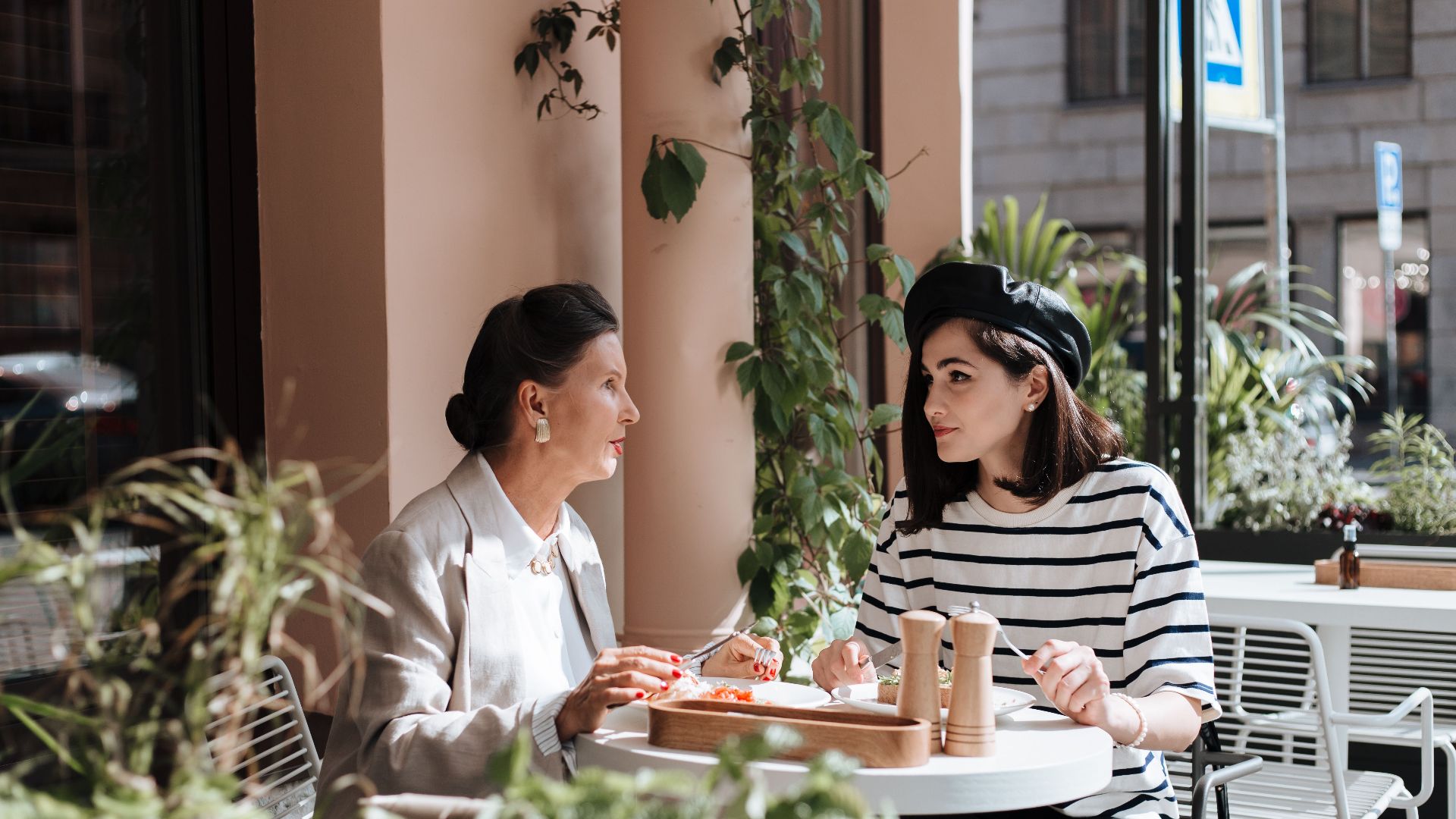 Two women enjoying lunch at an outdoor cafe, surrounded by greenery.