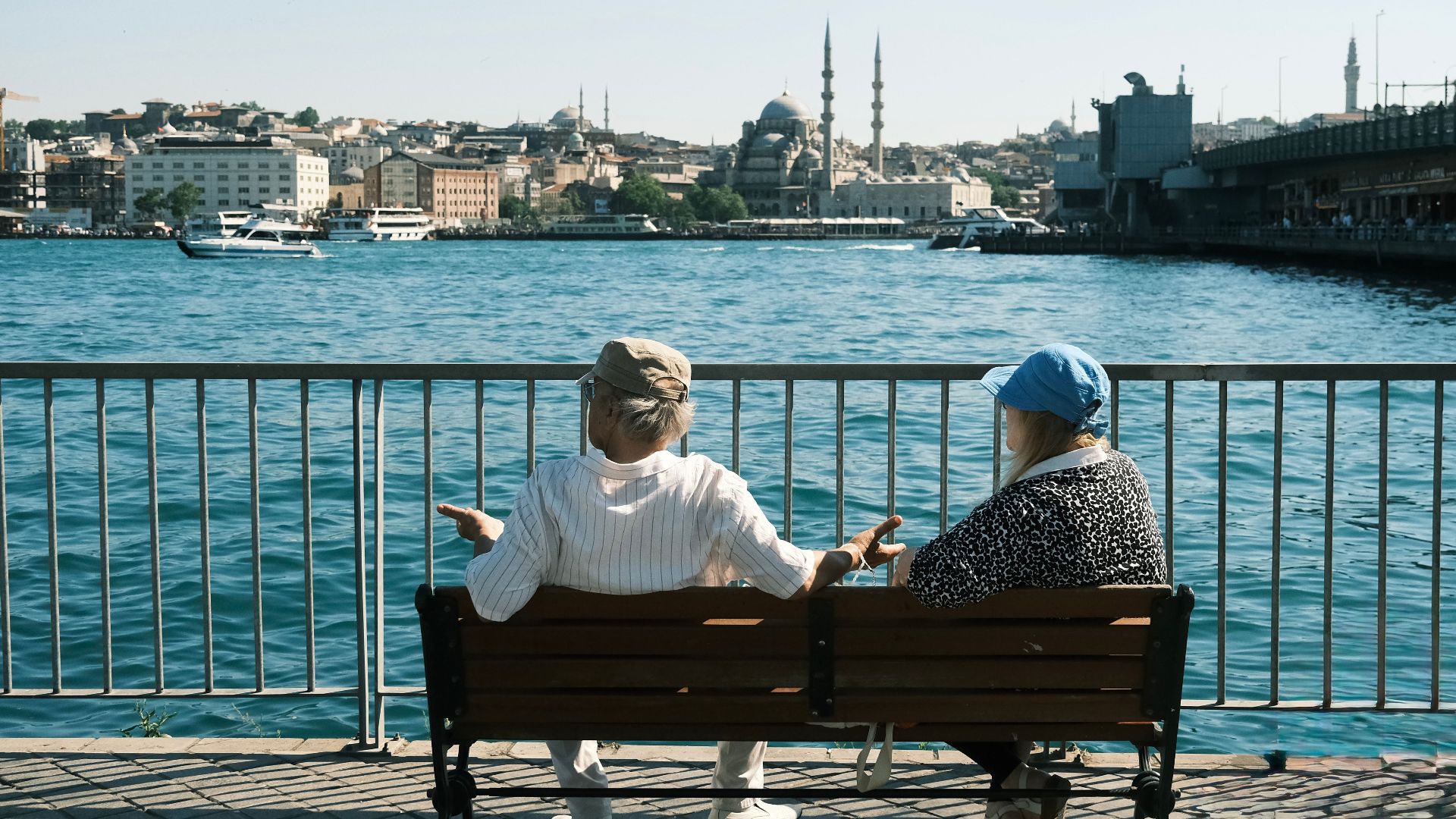 Elderly couple enjoys a sunny day by Istanbul's scenic waterfront with mosque view.