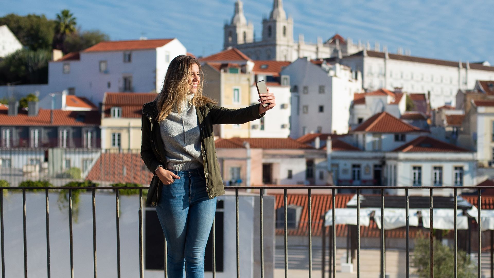A woman takes a selfie with the scenic backdrop of Lisbon architecture.