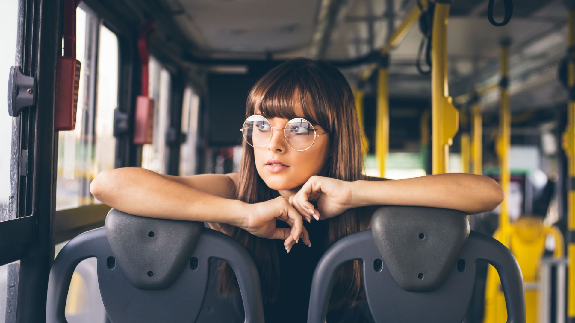 Stylish young woman with glasses poses inside a bus, showcasing fashion and travel style.