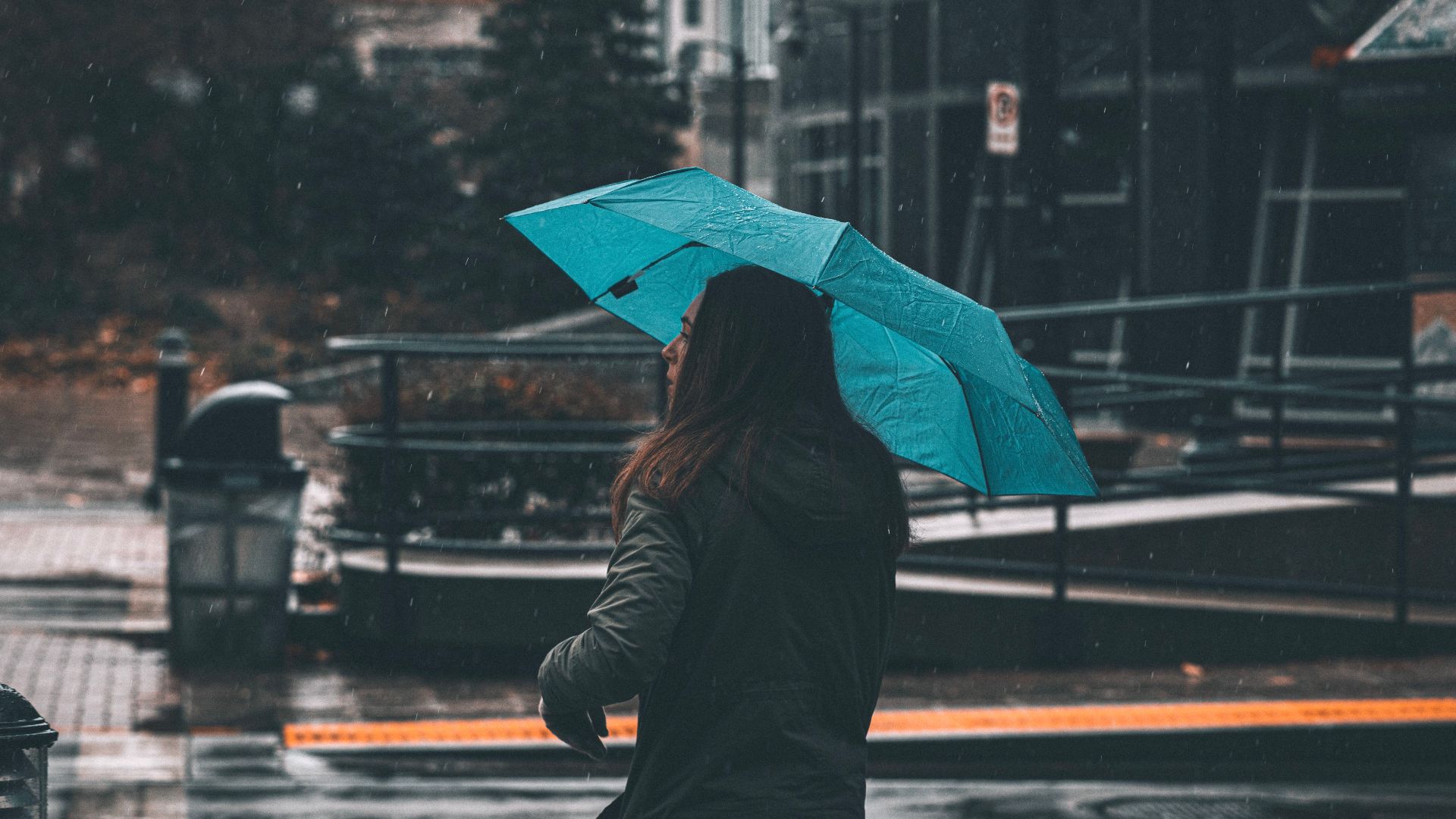 A woman with a blue umbrella walks through a city street on a rainy day, capturing the essence of urban life.